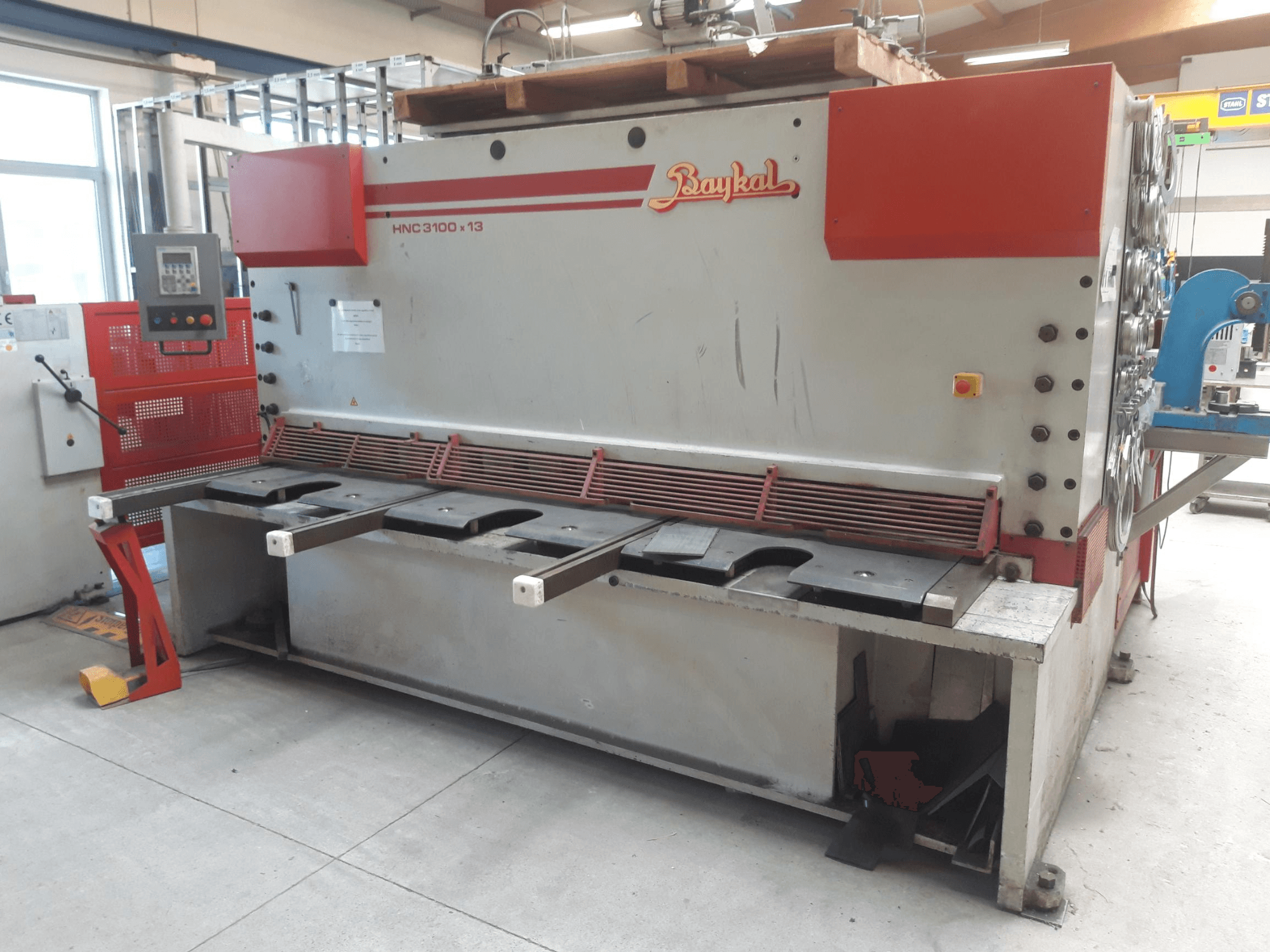 Vista frontale della cesoia CNC Baykal HNC 3100x13, con pannello di controllo, area di taglio del metallo e vano di raccolta degli scarti.