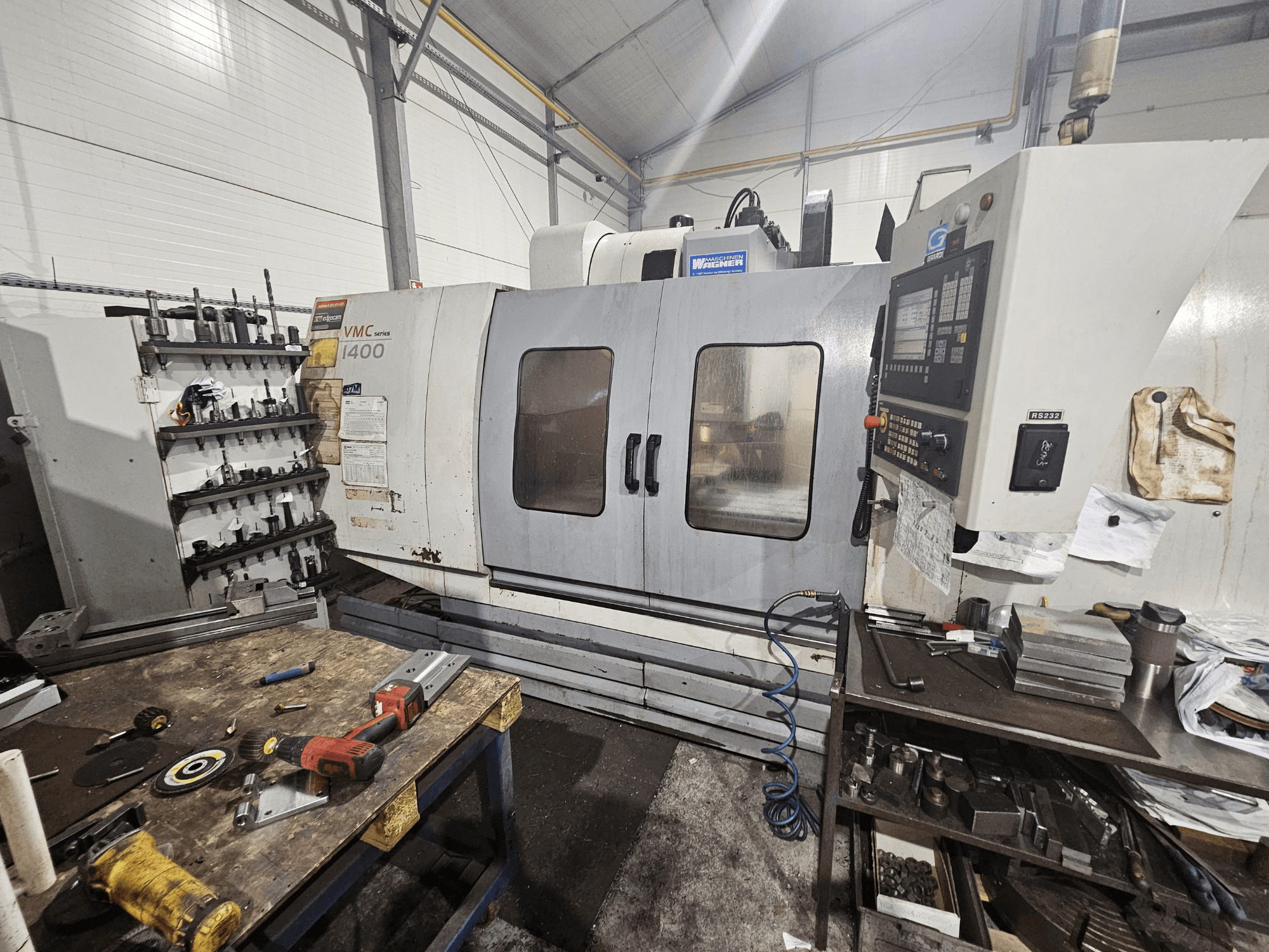 Fresatrice CNC VMC 1400 in un'officina, vista frontale; utensili e materiali sparsi sul banco di lavoro vicino.