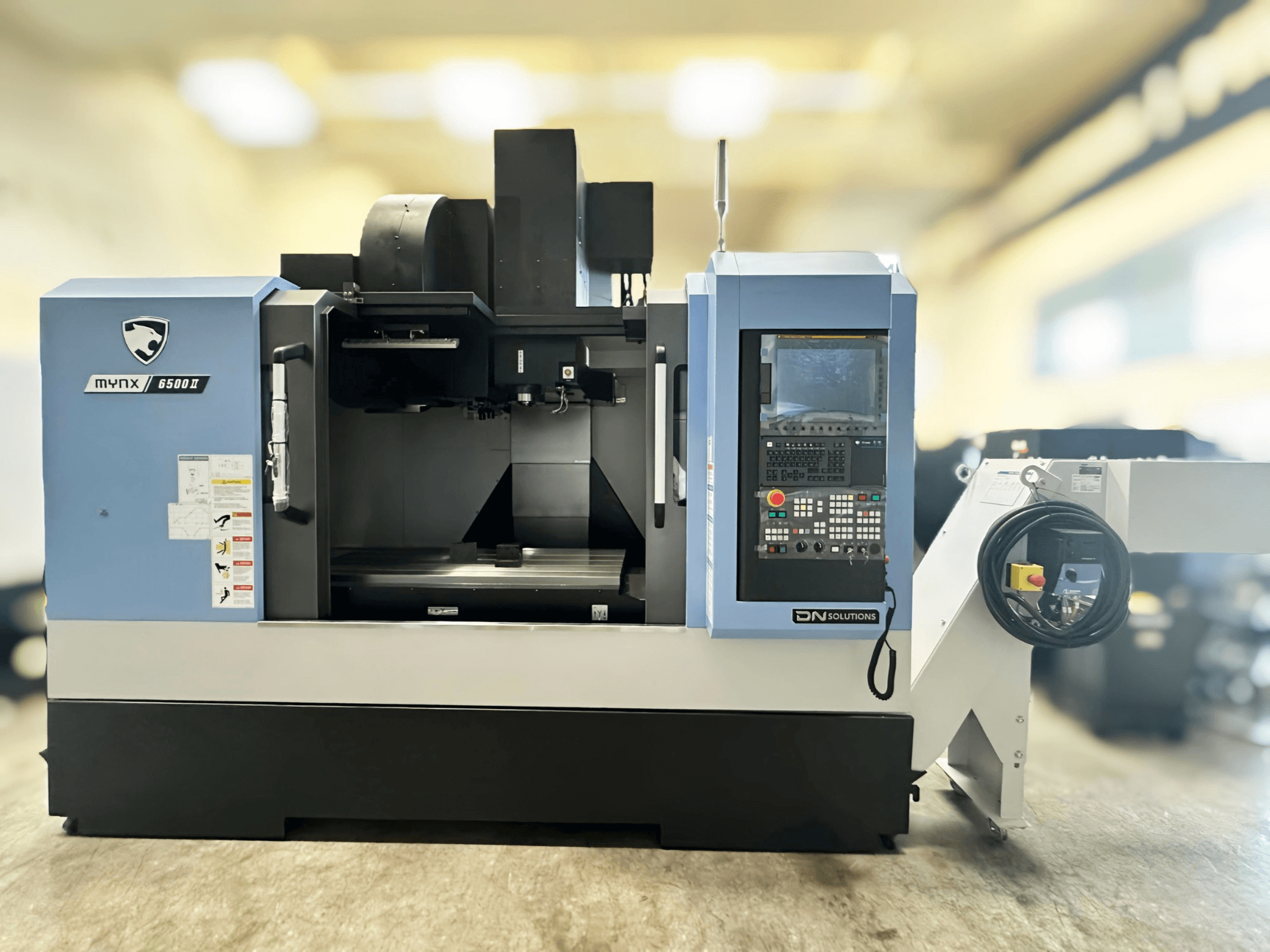 Centro di lavorazione verticale DN SOLUTIONS MYNX 6500 II visto frontalmente, con pannello di controllo e interfaccia operativa.