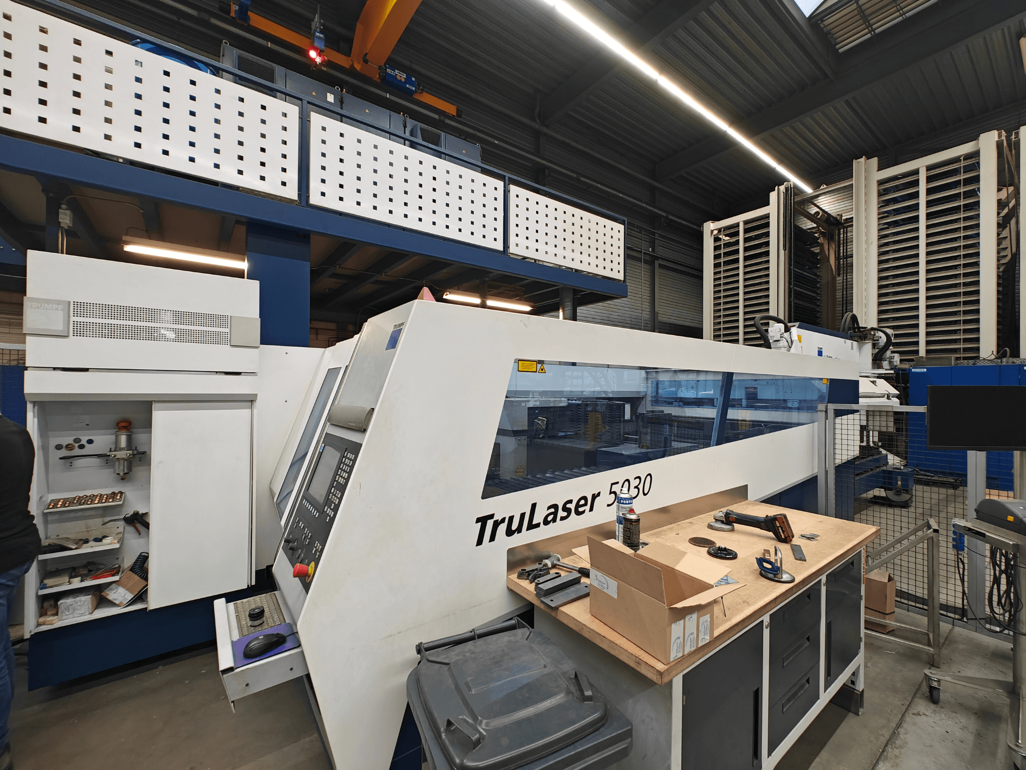 Macchina TruLaser 5030 in un'officina, vista frontale con pannello di controllo visibile, circondata da strumenti e attrezzature.