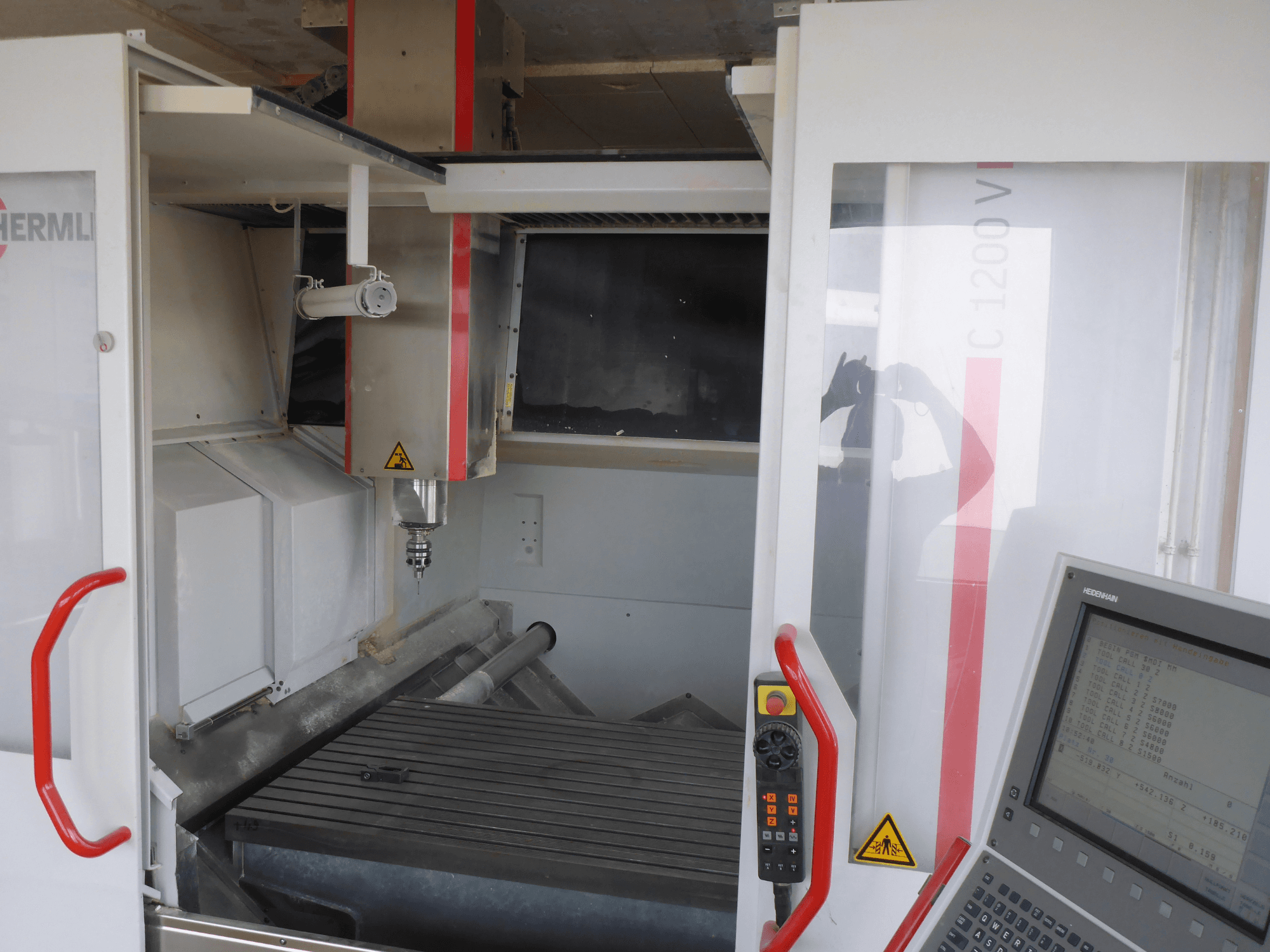 L'interno del centro di lavoro verticale HERMLE C 1200 mostra il portautensili, il pannello di controllo e il piano di lavoro da una vista frontale.