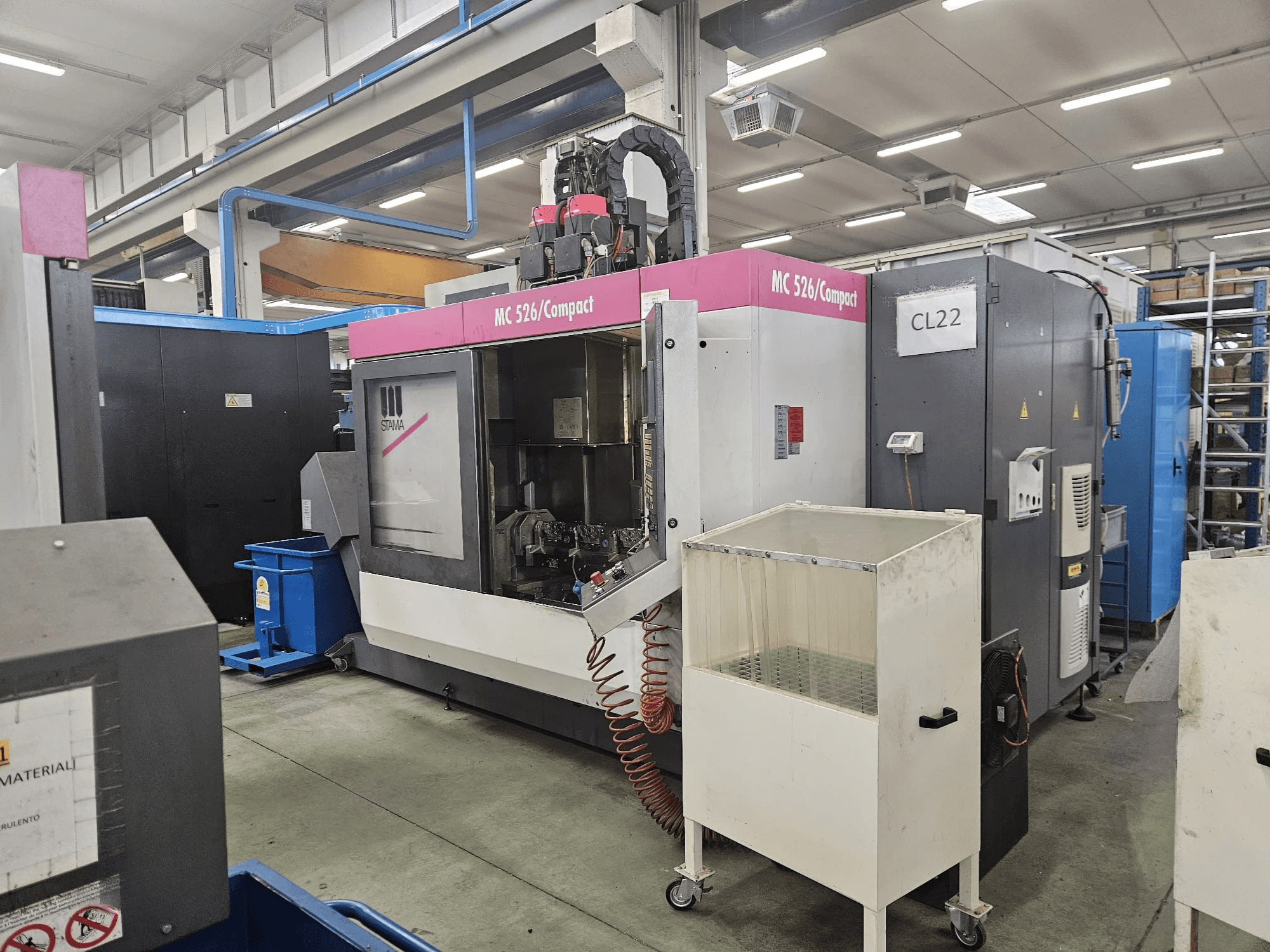 Macchina CNC compatta MC 526 di Stama, vista laterale, che mostra il pannello di controllo, il serbatoio del refrigerante e i macchinari adiacenti.