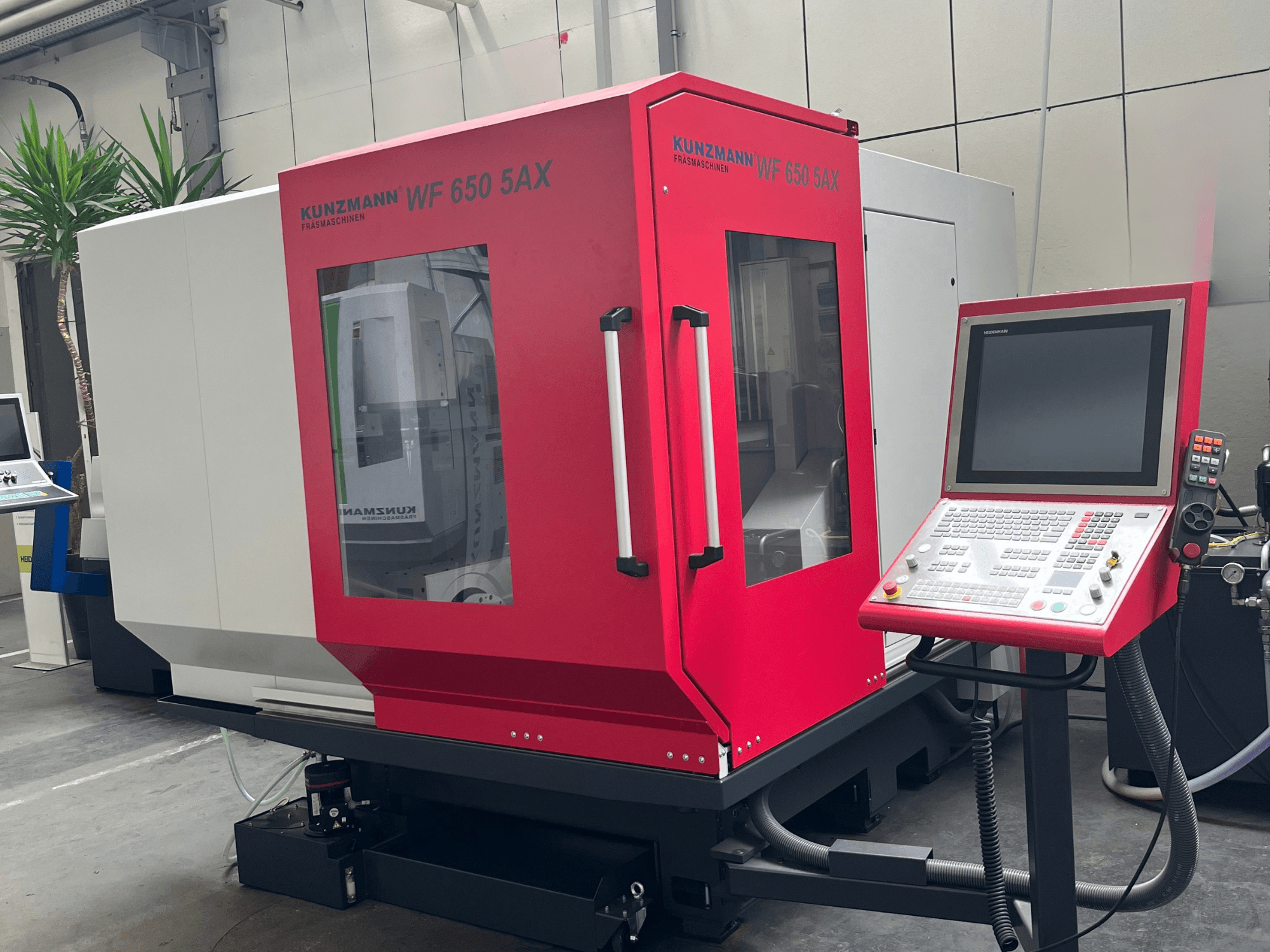 Centro di lavorazione verticale KUNZMANN WF 650 5AX di colore rosso, vista frontale con pannello di comando e touch screen, situato in un'officina.