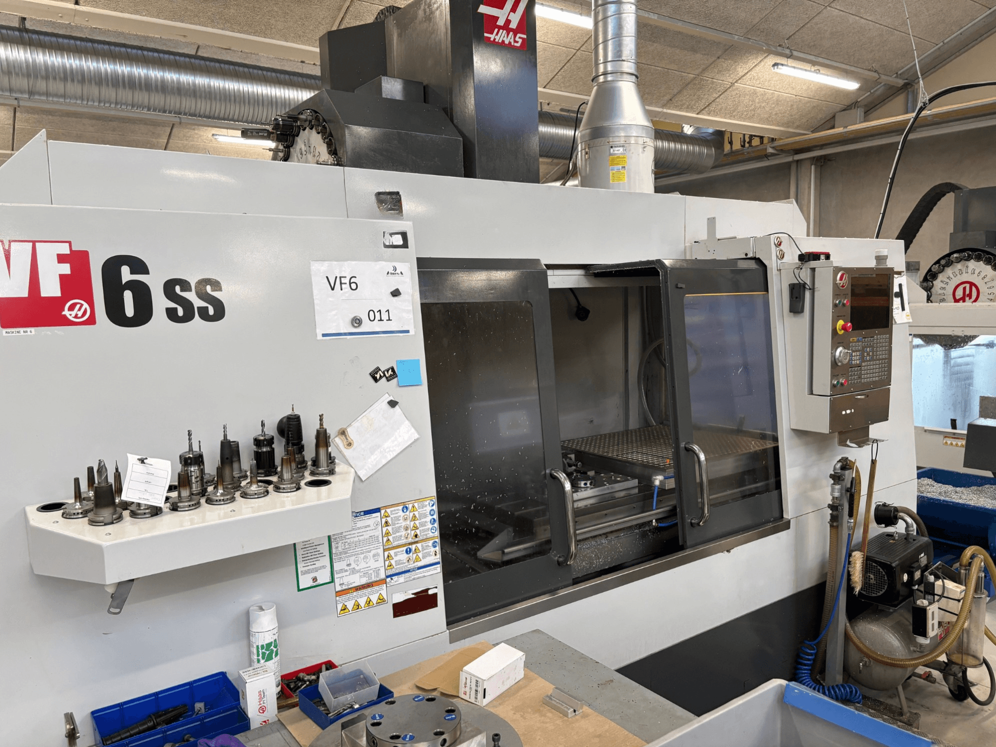 Fresatrice CNC Haas VF-6 SS, vista frontale. Presenta vari utensili, pannello di controllo e spazio di lavoro interno visibile.