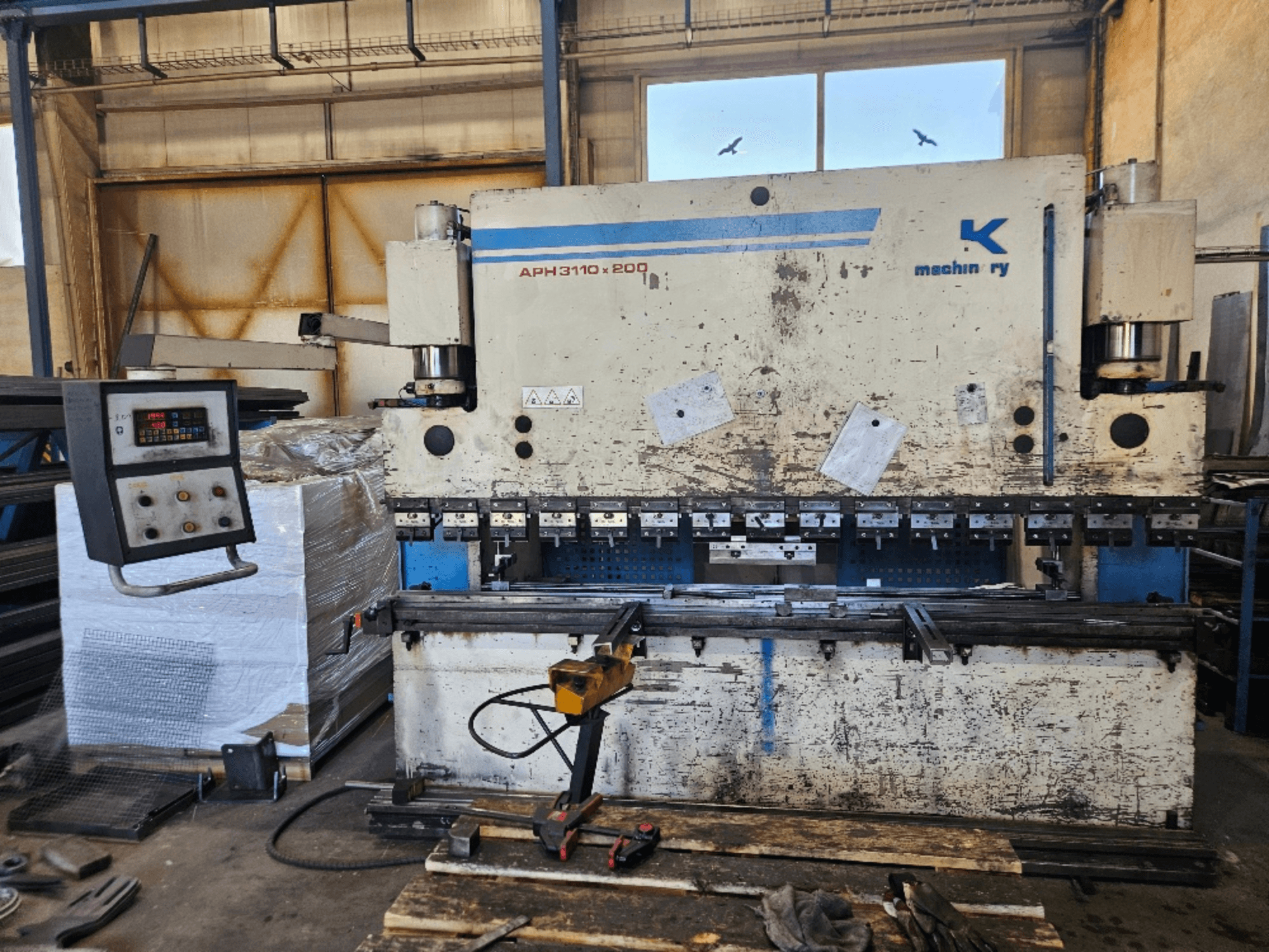 Pressa piegatrice Baykal APH 3110x200 in un'officina, vista frontale, con pannello di controllo, lamiere e utensili visibili.