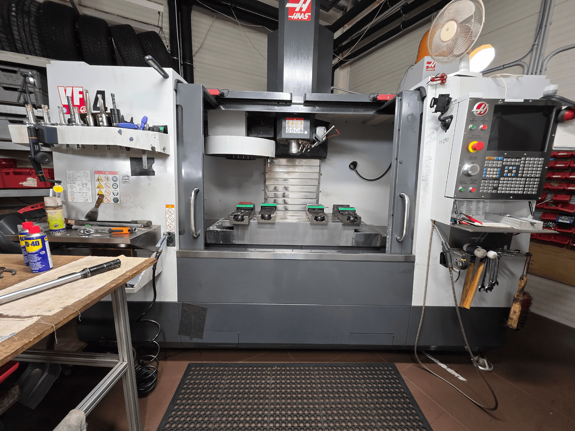 Vista frontale della fresa CNC Haas VF-4 in un'officina, con utensili, interfaccia del computer e due pezzi sul tavolo.