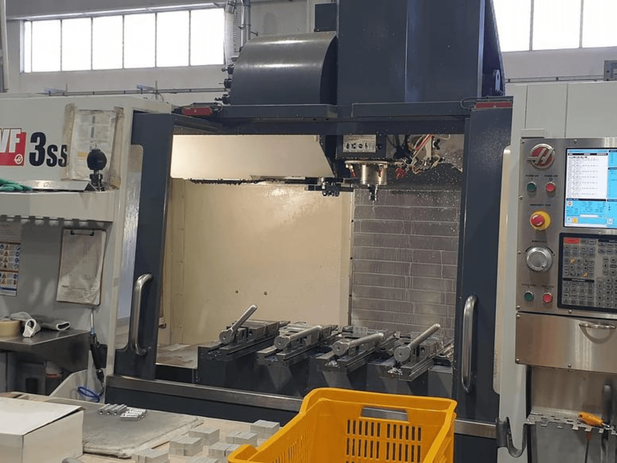 Centro di lavoro verticale HAAS VF-3SS, vista frontale con pannello di controllo CNC, utensili e cesto arancione.