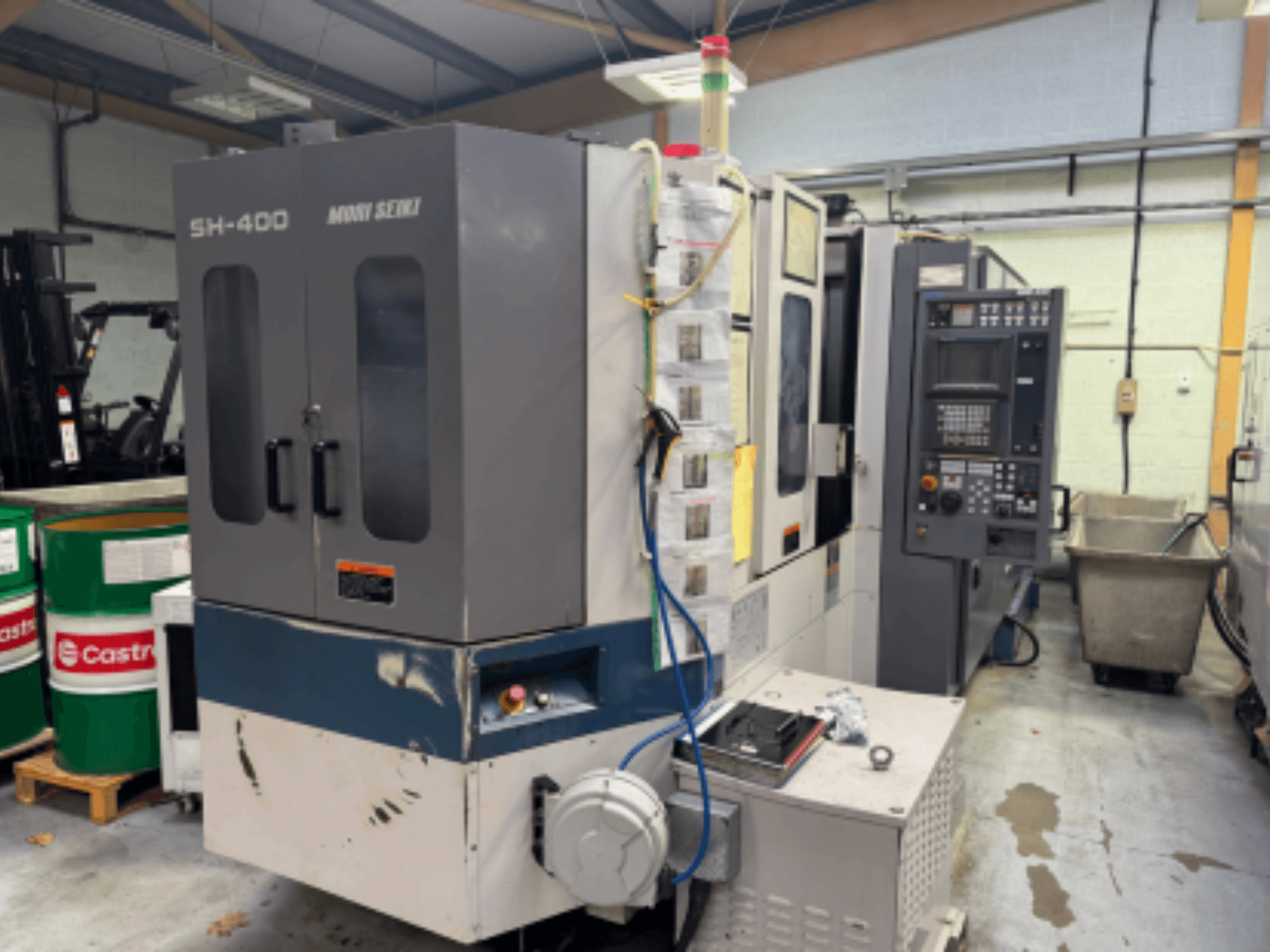 Macchina CNC Moni Seiki SH-400, vista laterale che mostra il pannello di controllo, le porte e l'ambiente industriale circostante.