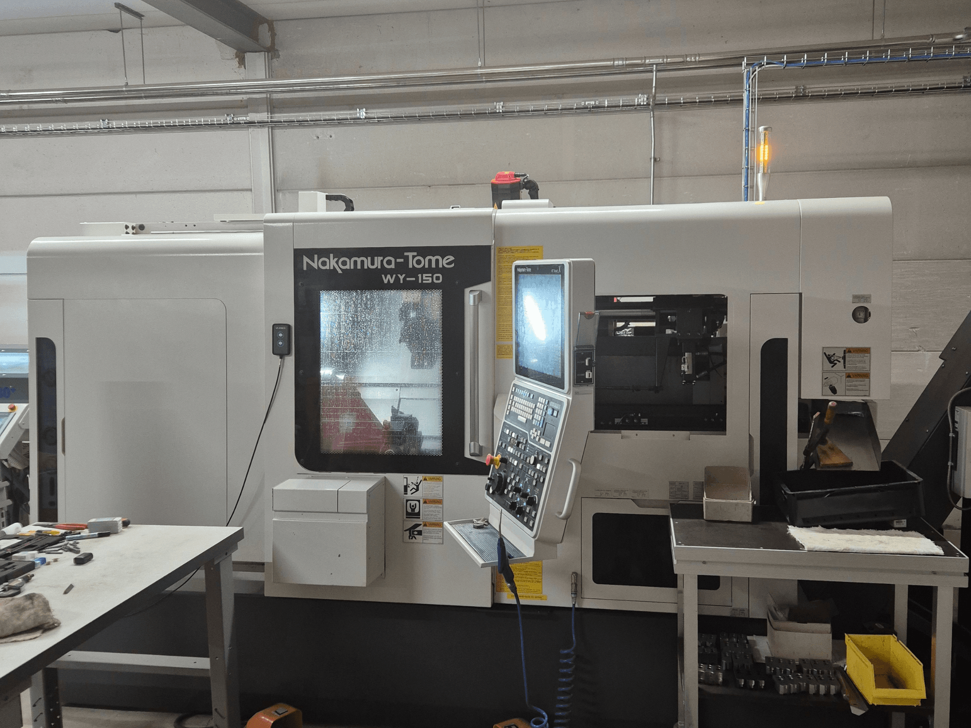 Tornio CNC Nakamura-Tome WY-150 in vista laterale, con pannello di controllo, finestra trasparente e area di lavoro visibile.