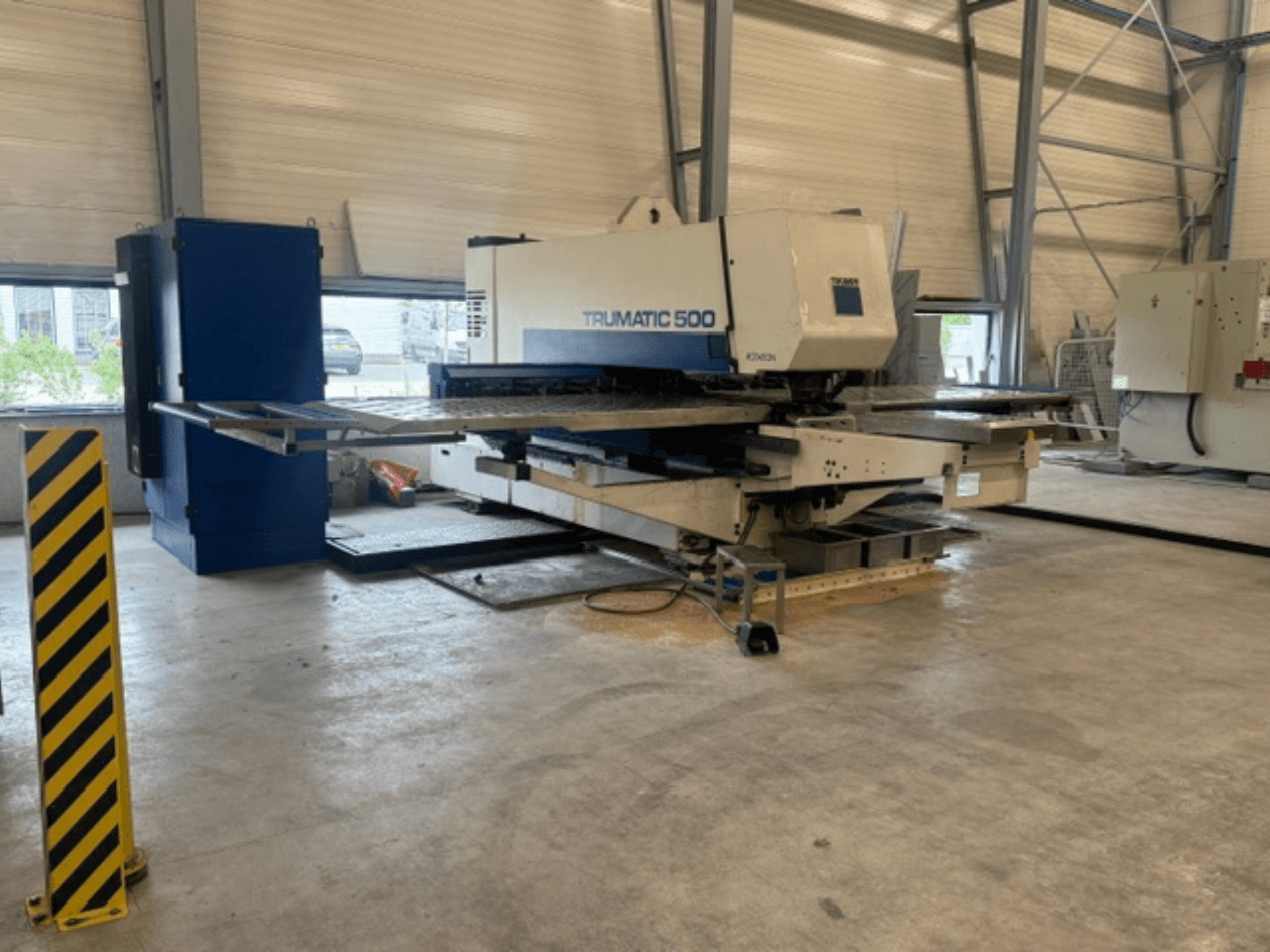 Punzonatrice CNC TRUMPF Trumatic 500 in un'officina; vista laterale che mostra il macchinario e il palo di sicurezza con strisce gialle.
