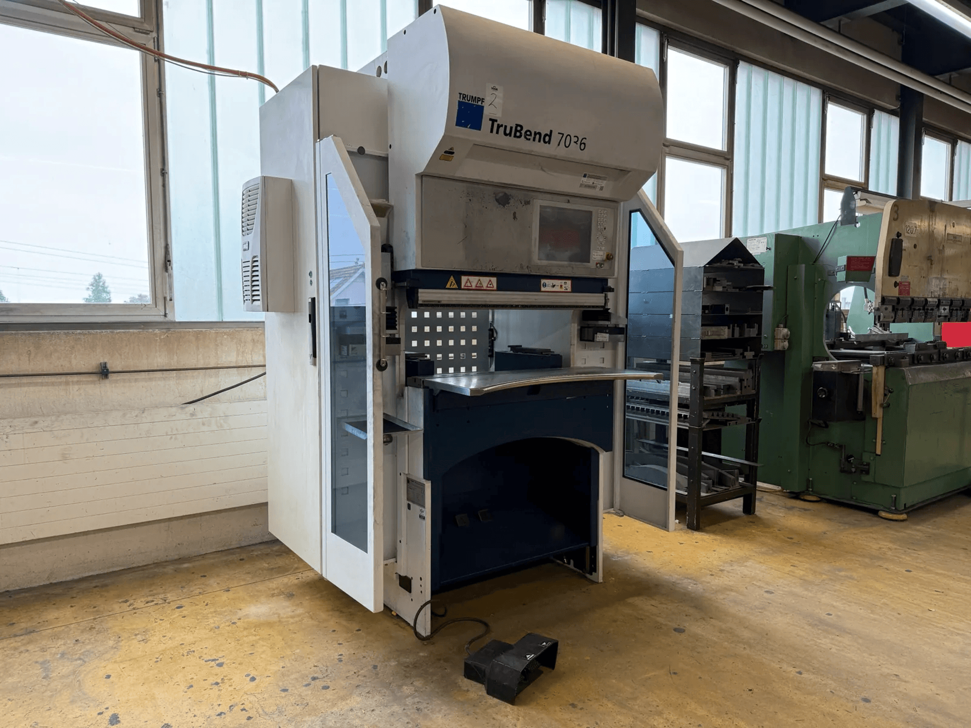 Piegatrice TRUMPF TruBend 7036 in un'officina, vista frontale con lo sportello aperto, che mostra il pannello di controllo e l'area di piegatura.