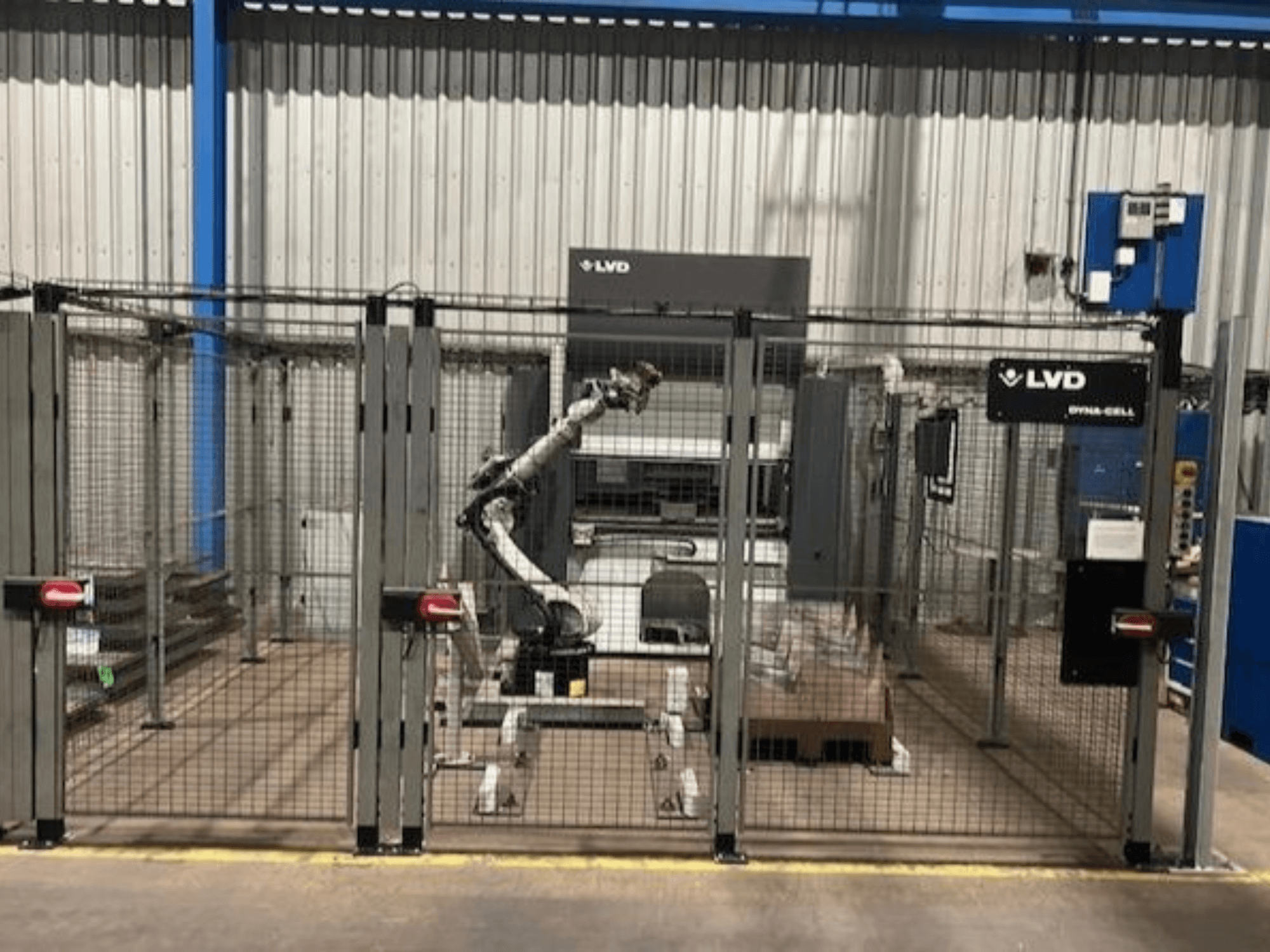 Stazione di lavoro robotica LVD Dyna-Cell in un recinto, vista frontale, con braccio robotico e pannello di controllo.