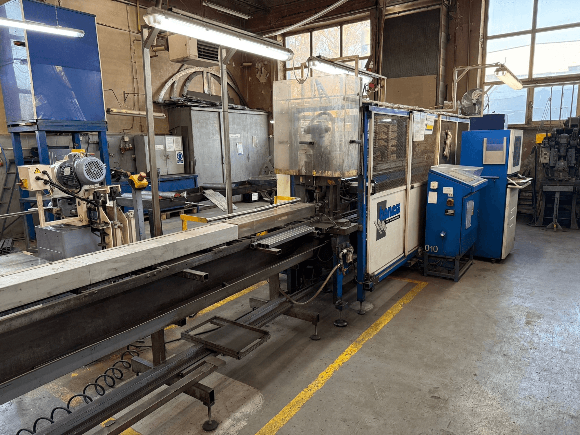 Officina industriale con una macchina Haweas blu, vista laterale che mostra il trasportatore e le attrezzature in uno spazio ampio e ben illuminato.