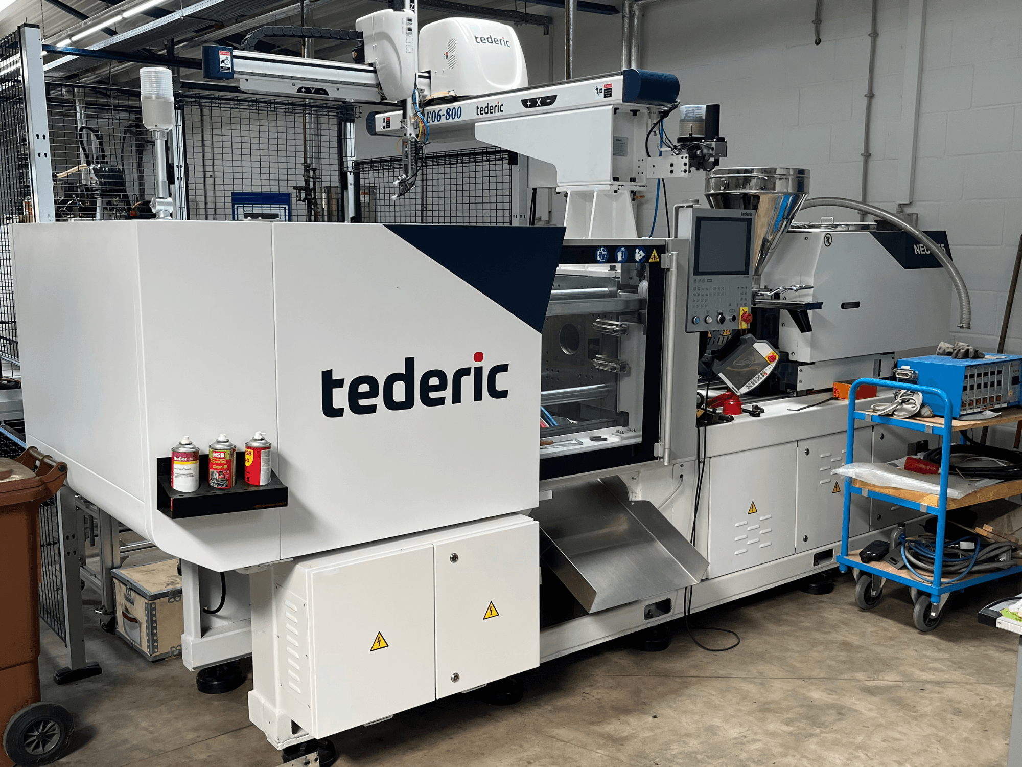 Macchina per lo stampaggio a iniezione idraulica TEDERIC NEO.E55/e110h in un'officina, vista laterale con pannello di controllo e utensili adiacenti.