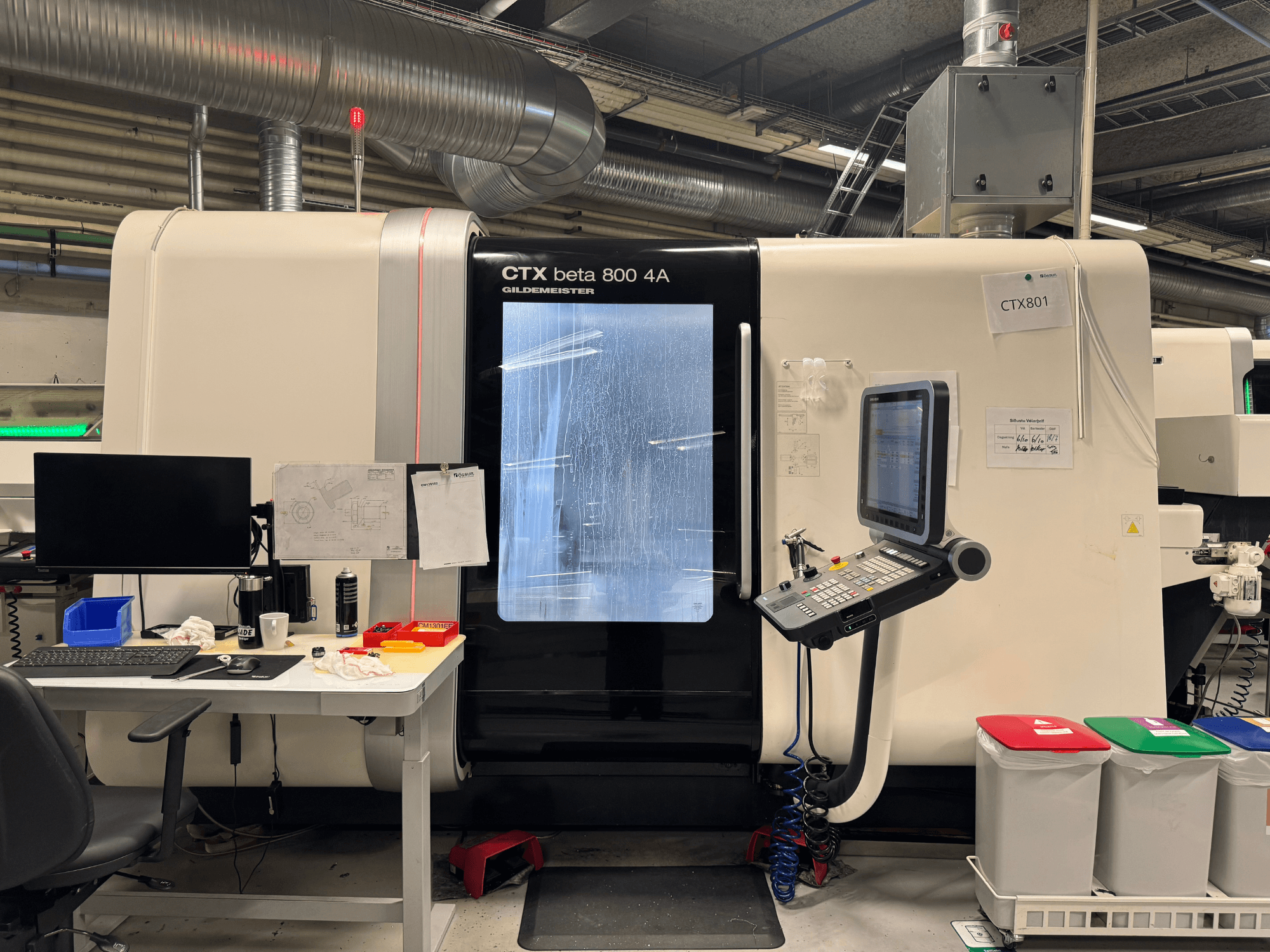 Macchina CTX beta 800 4A con pannello di controllo e monitor, vista laterale, in un'officina con allestimento ufficio e cestini colorati.