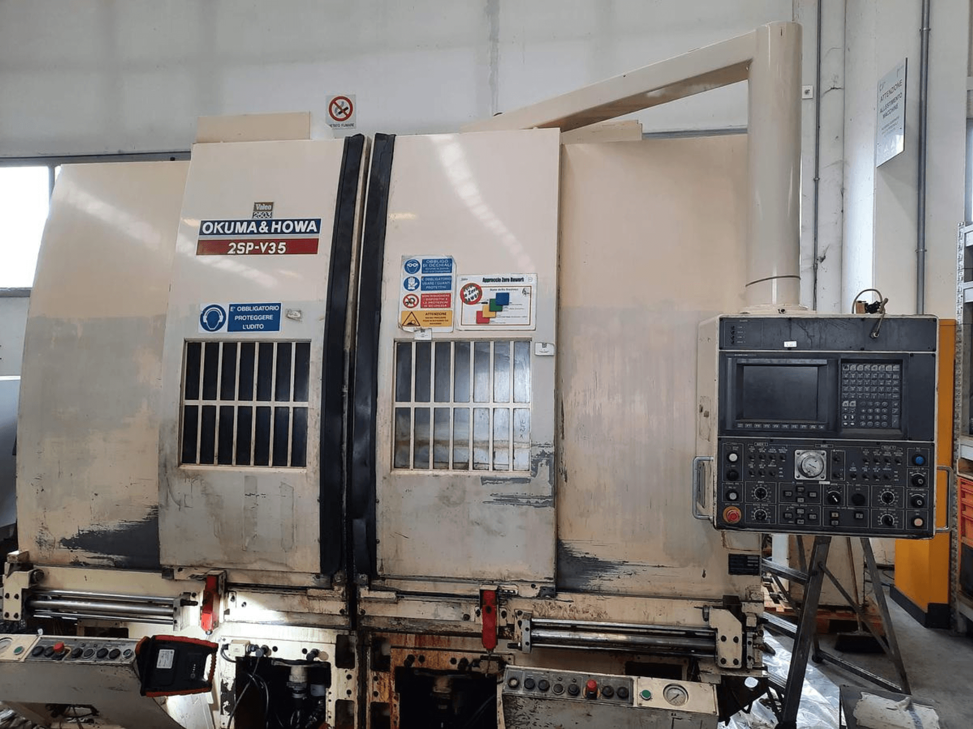Macchina CNC OKUMA & HOWA 2SP-V35 vista dal davanti, con pannello di controllo con vari pulsanti ed etichette di sicurezza.