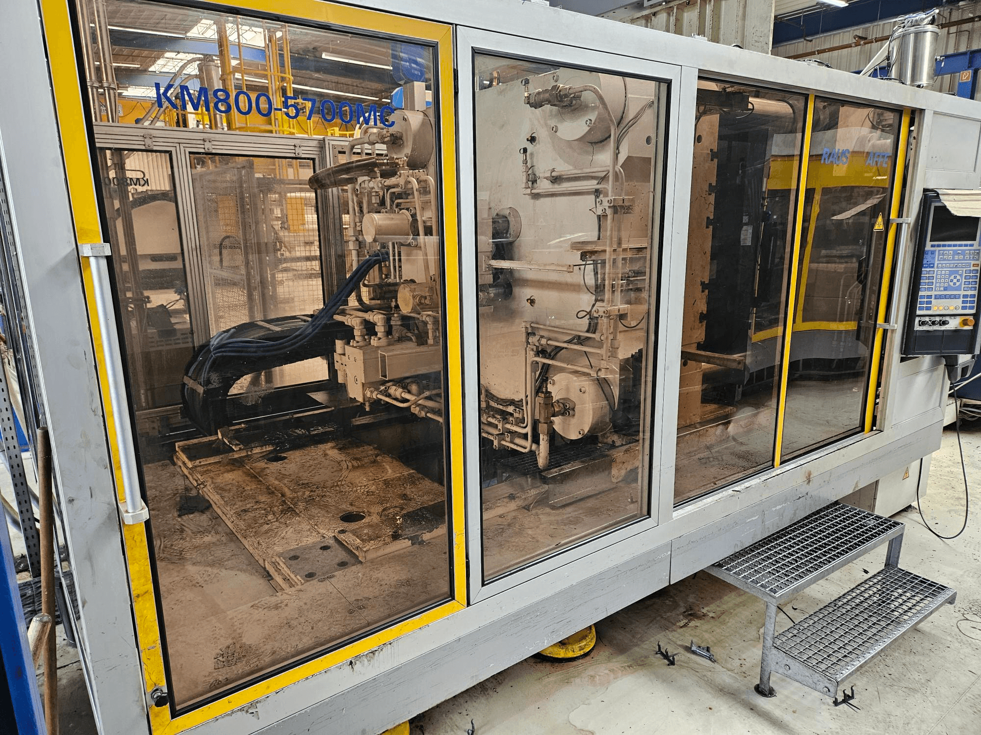 Macchina per lo stampaggio a iniezione idraulica Krauss Maffei KM800-5700 MC, vista frontale che mostra i componenti attraverso i pannelli di vetro.