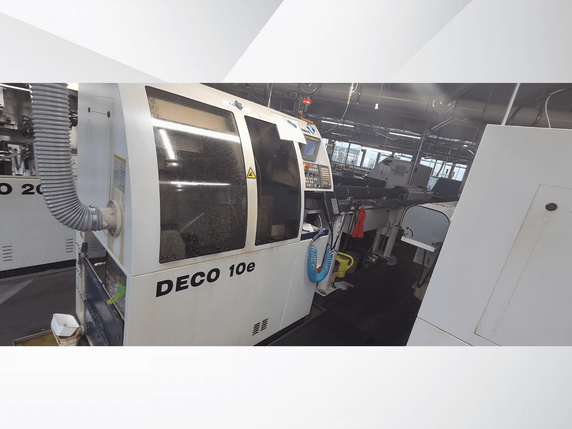 Macchina DECO 10e in un'officina; vista laterale che mostra il pannello di controllo e il tubo di ventilazione, con macchinari sfocati sullo sfondo.