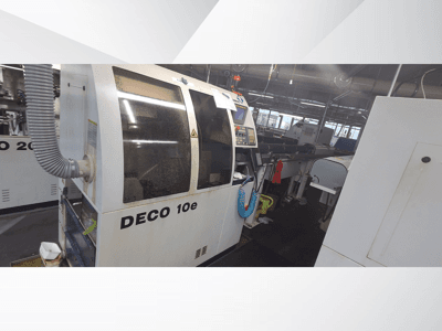 Macchina DECO 10e in un'officina; vista laterale che mostra il pannello di controllo e il tubo di ventilazione, con macchinari sfocati sullo sfondo.