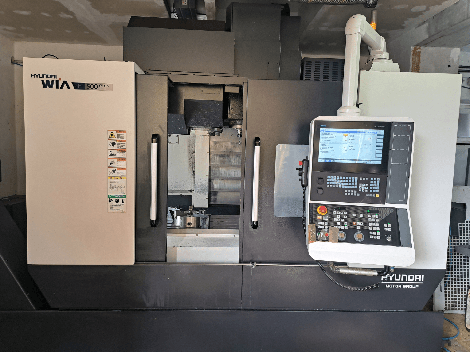 Macchina CNC Hyundai WIA F500 Plus in vista frontale, con pannello di controllo digitale ed etichette di sicurezza.