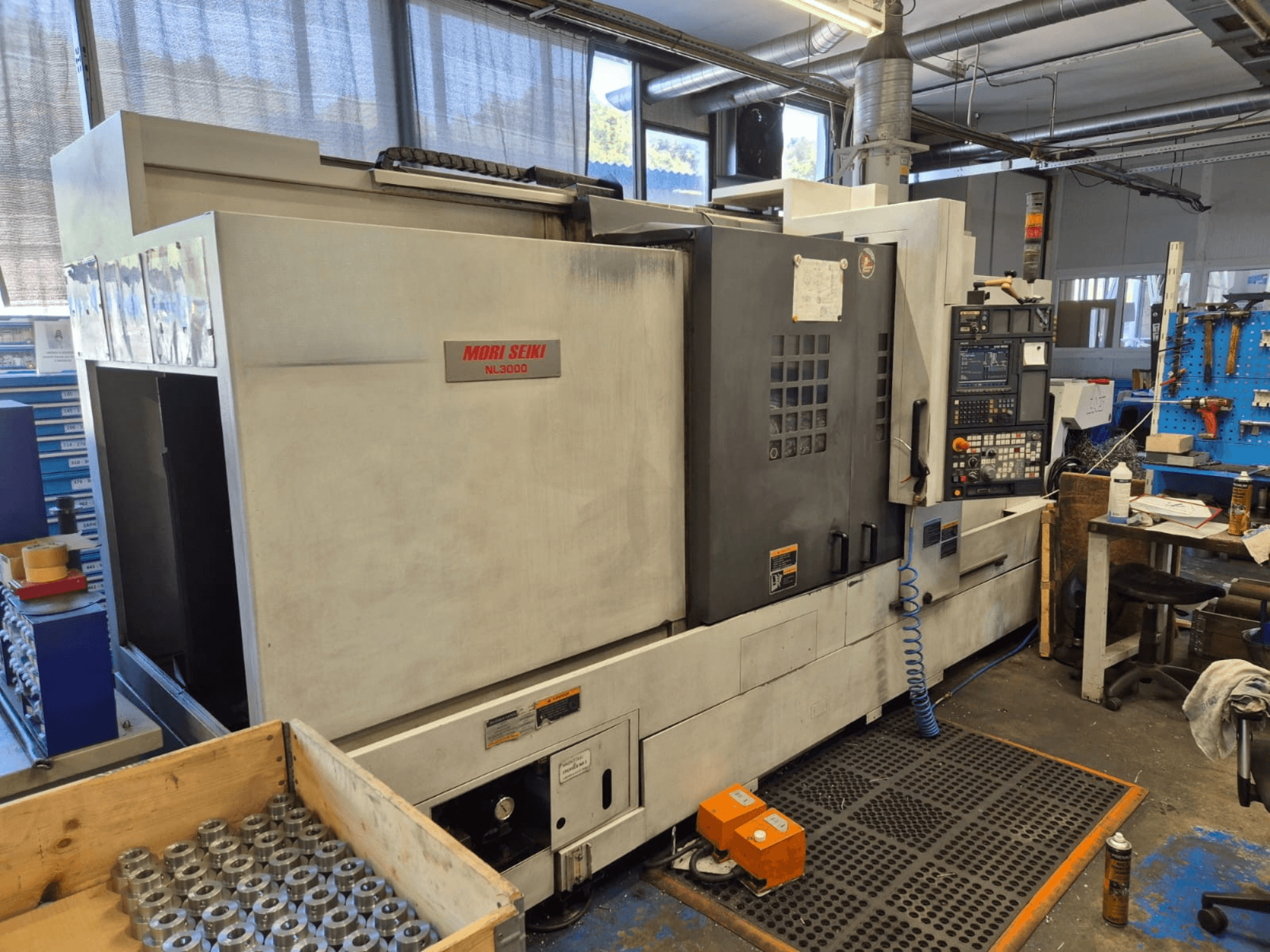Tornio CNC Mori Seiki NL3000 in un'officina, vista laterale che mostra il pannello di controllo, gli utensili e le parti metalliche in una scatola di legno.