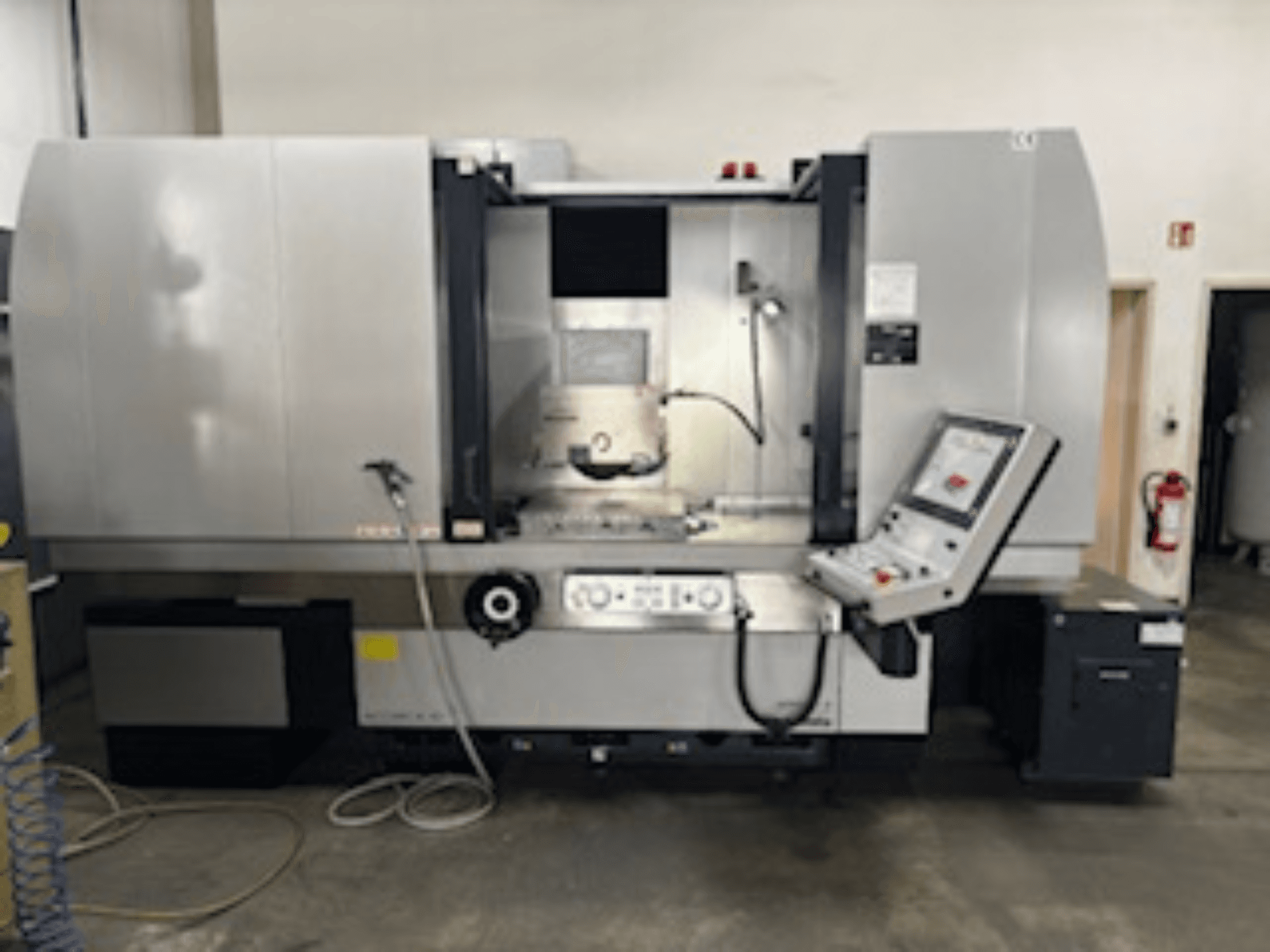 Vista frontale della fresatrice CNC con pannello di controllo, sistema di raffreddamento visibile e area di lavorazione; marca e modello non specificati.
