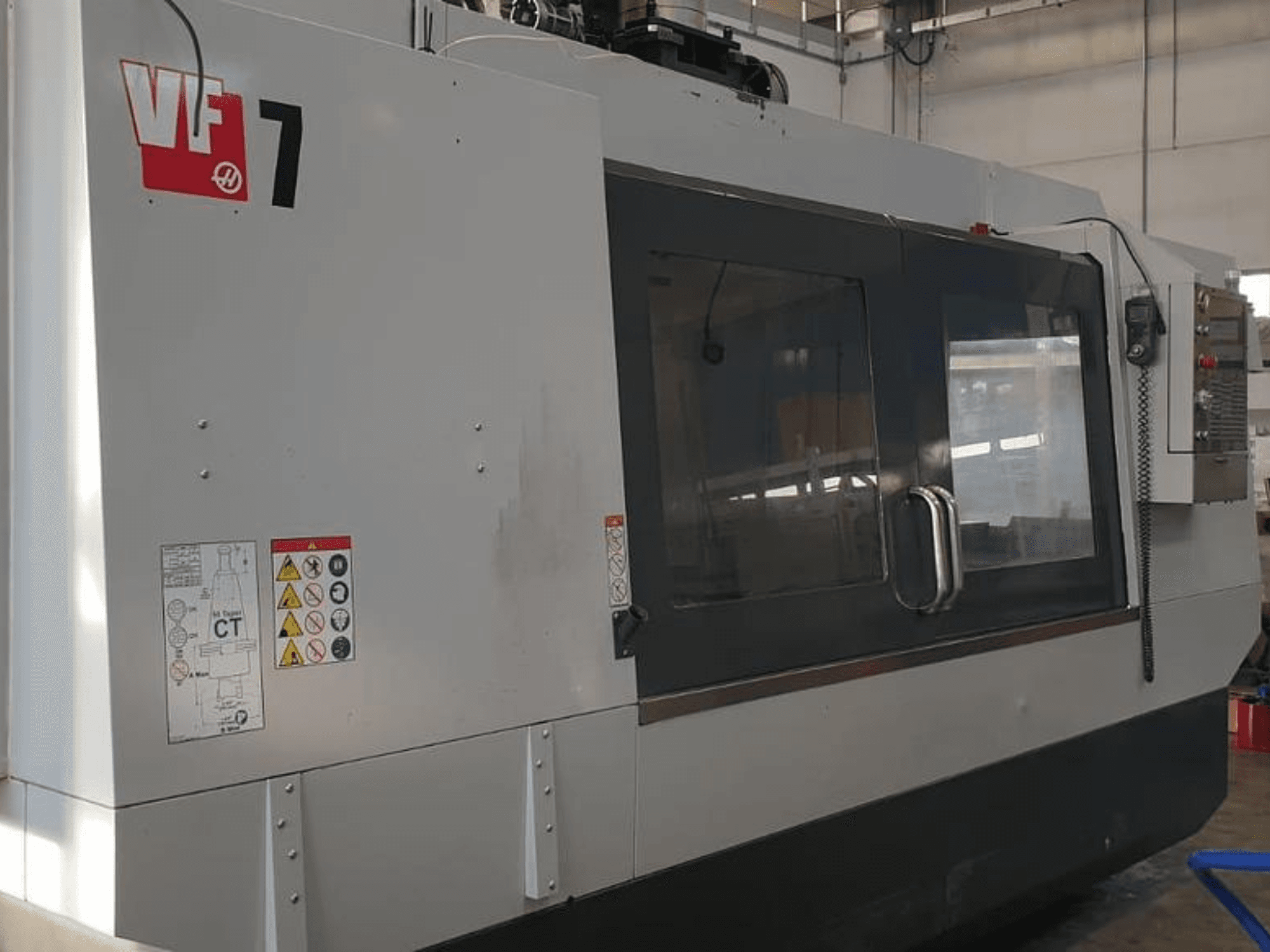 Macchina CNC Haas VF-7 in vista laterale, con finitura grigio metallo, pannello di controllo ed etichette di sicurezza.