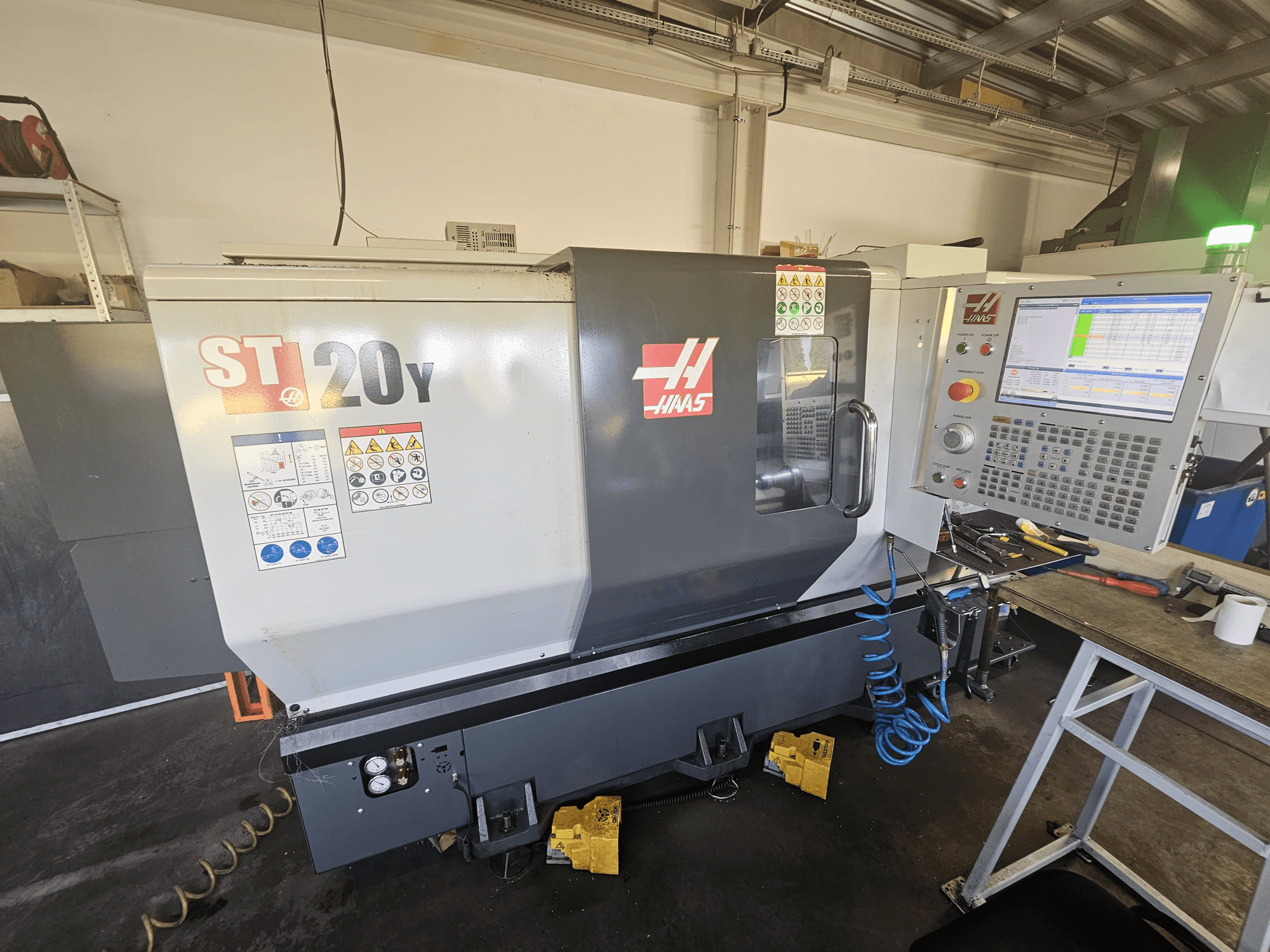 Tornio CNC Haas ST-20Y in vista frontale con pannello di controllo; include etichette di sicurezza e dettagli del tubo dell'aria sul lato.