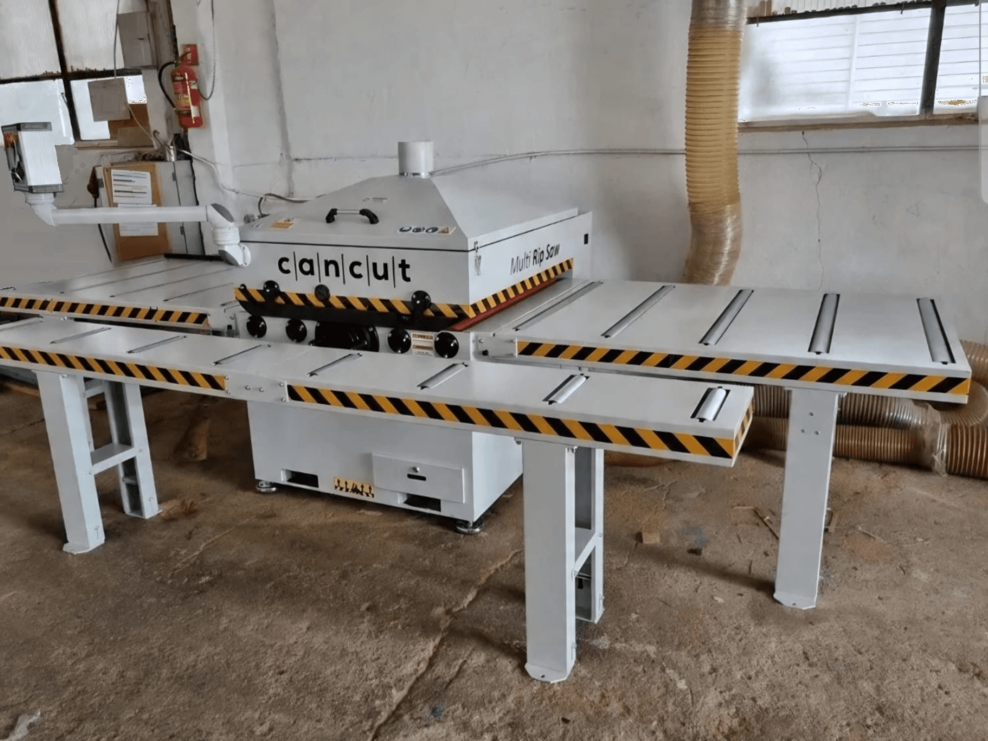 Sega circolare per legno CAN CUT MC 930 con doppio piano di lavoro dotato di strisce di sicurezza, vista frontale in un’officina al coperto.