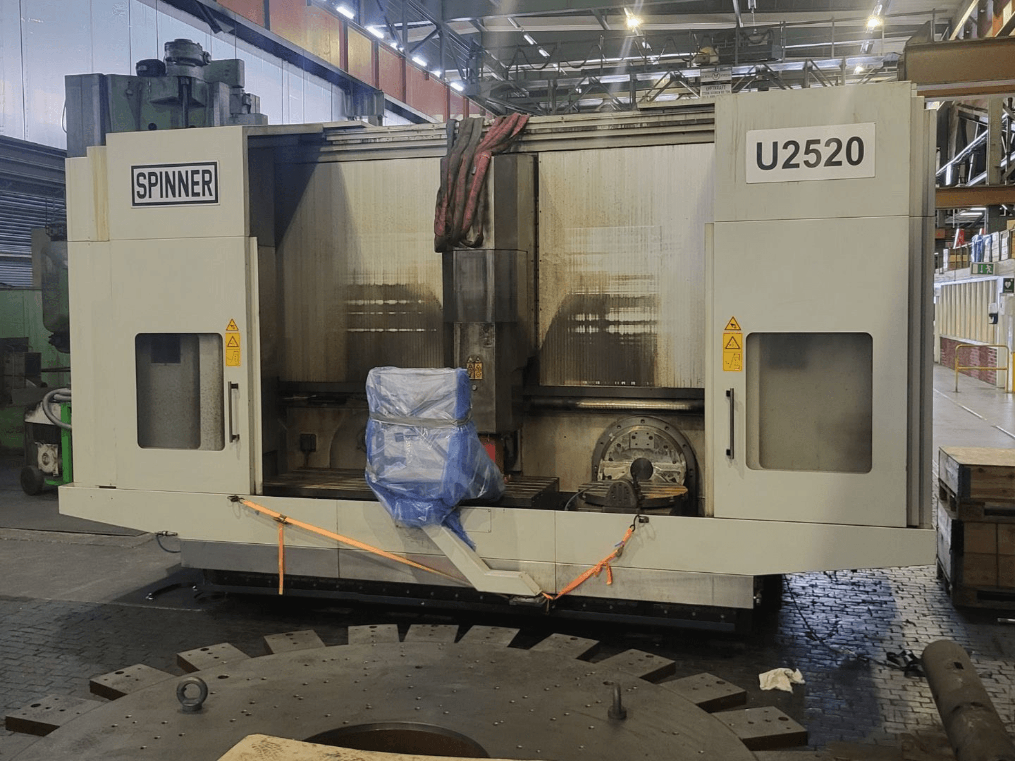 Centro di lavorazione verticale SPINNER U5-2520 visto frontalmente, con tavola coperta ed etichette di sicurezza.
