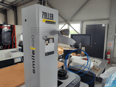 Dispositivo di misurazione ZOLLER smile 420 con monitor, vista laterale in un'officina, con tubi blu e macchinari sullo sfondo.