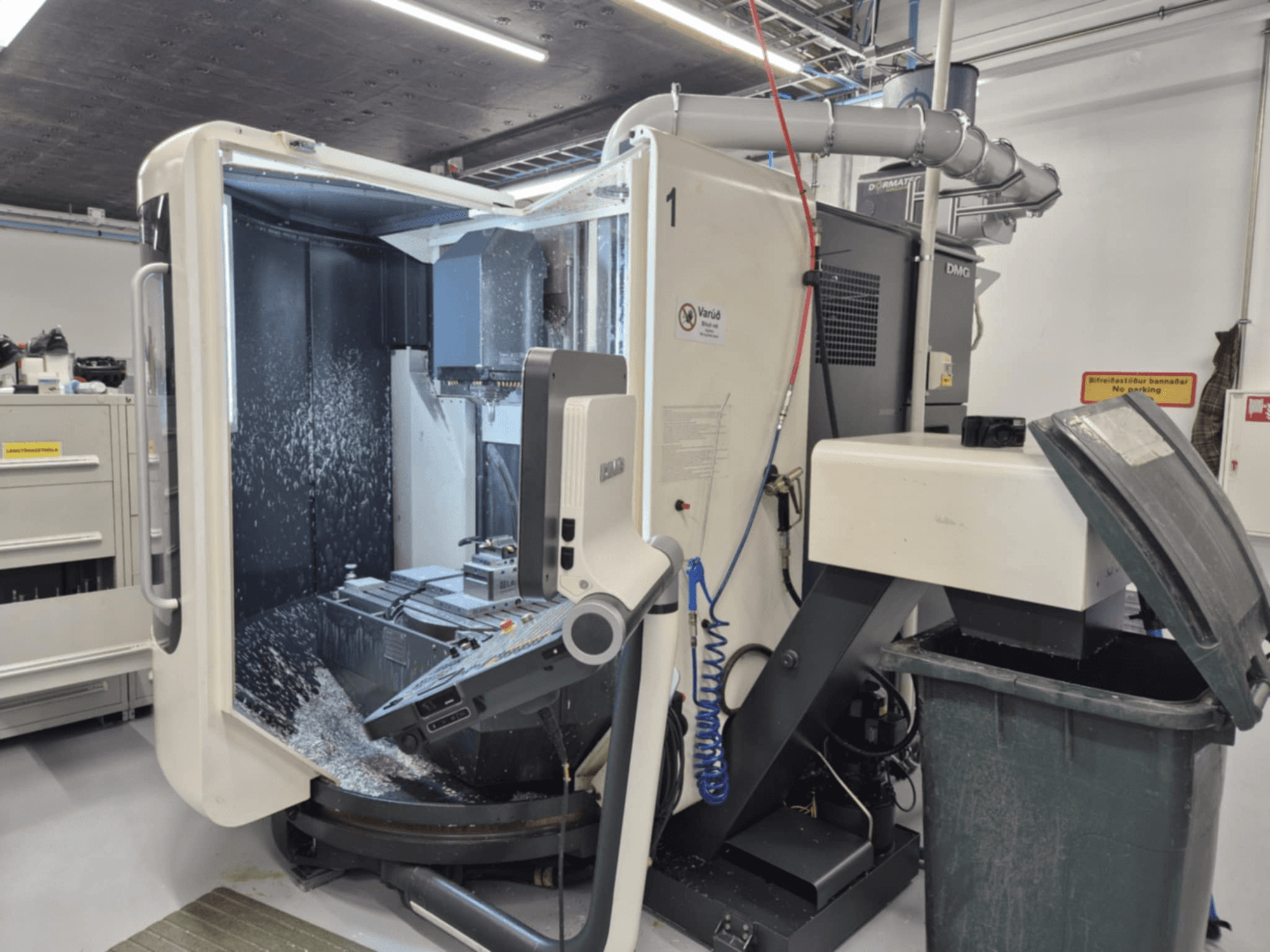 Fresatrice DMG aperta con spruzzi di refrigerante, che mostra trucioli di metallo e comandi degli utensili, vista dal davanti.