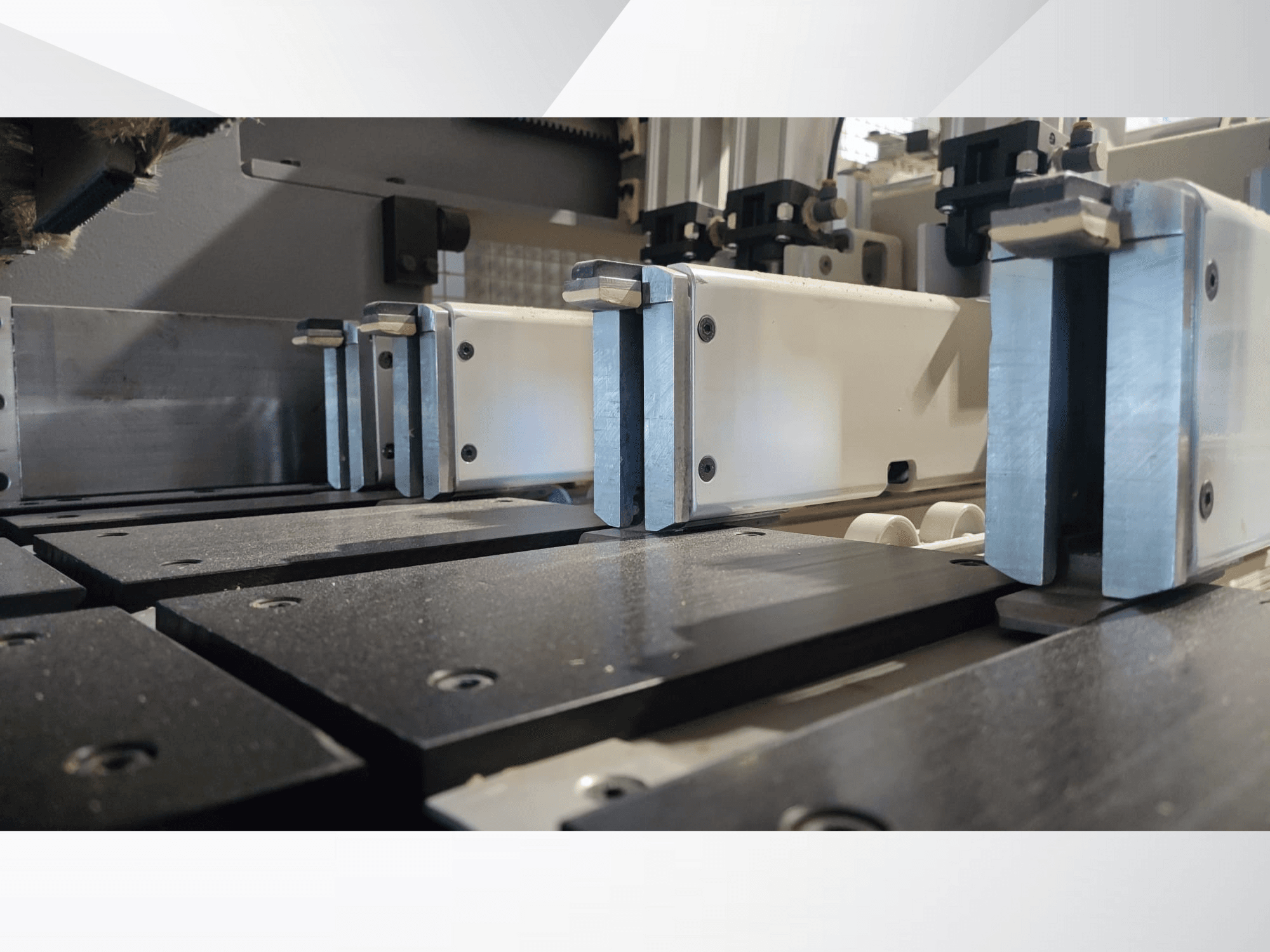 Vista ravvicinata del meccanismo di serraggio di una macchina di precisione con ganasce metalliche, con superfici di lavoro nere e guide visibili.