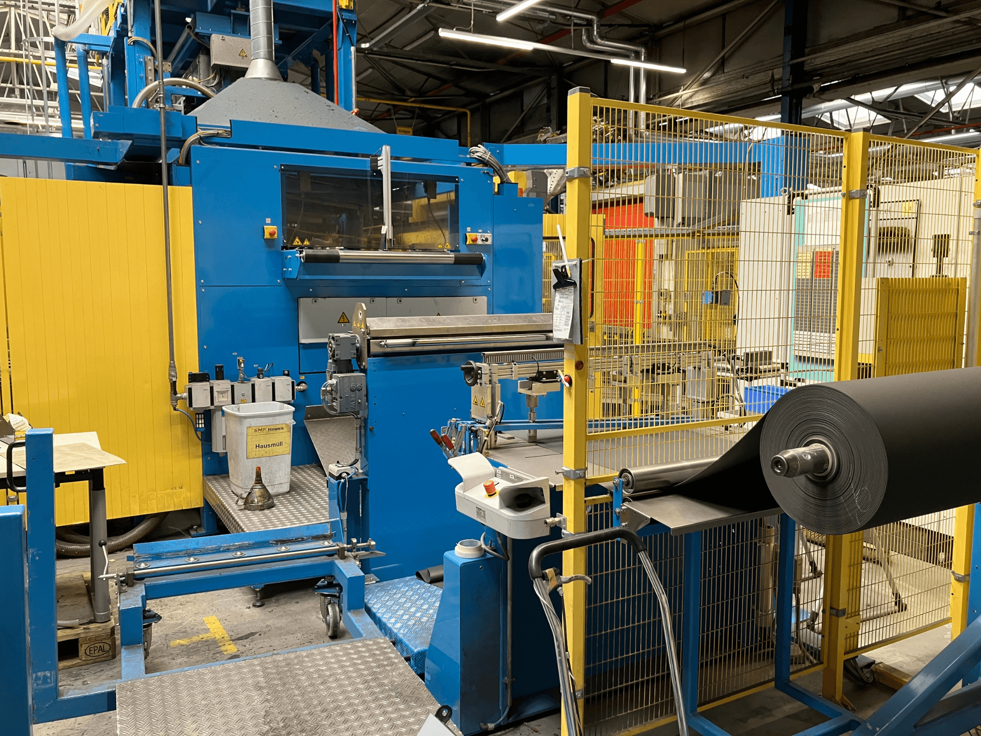 Macchina per la lavorazione della plastica KIEFEL KLS 86/235 vista frontalmente, con rotolo di materiale nero e pannello di controllo.