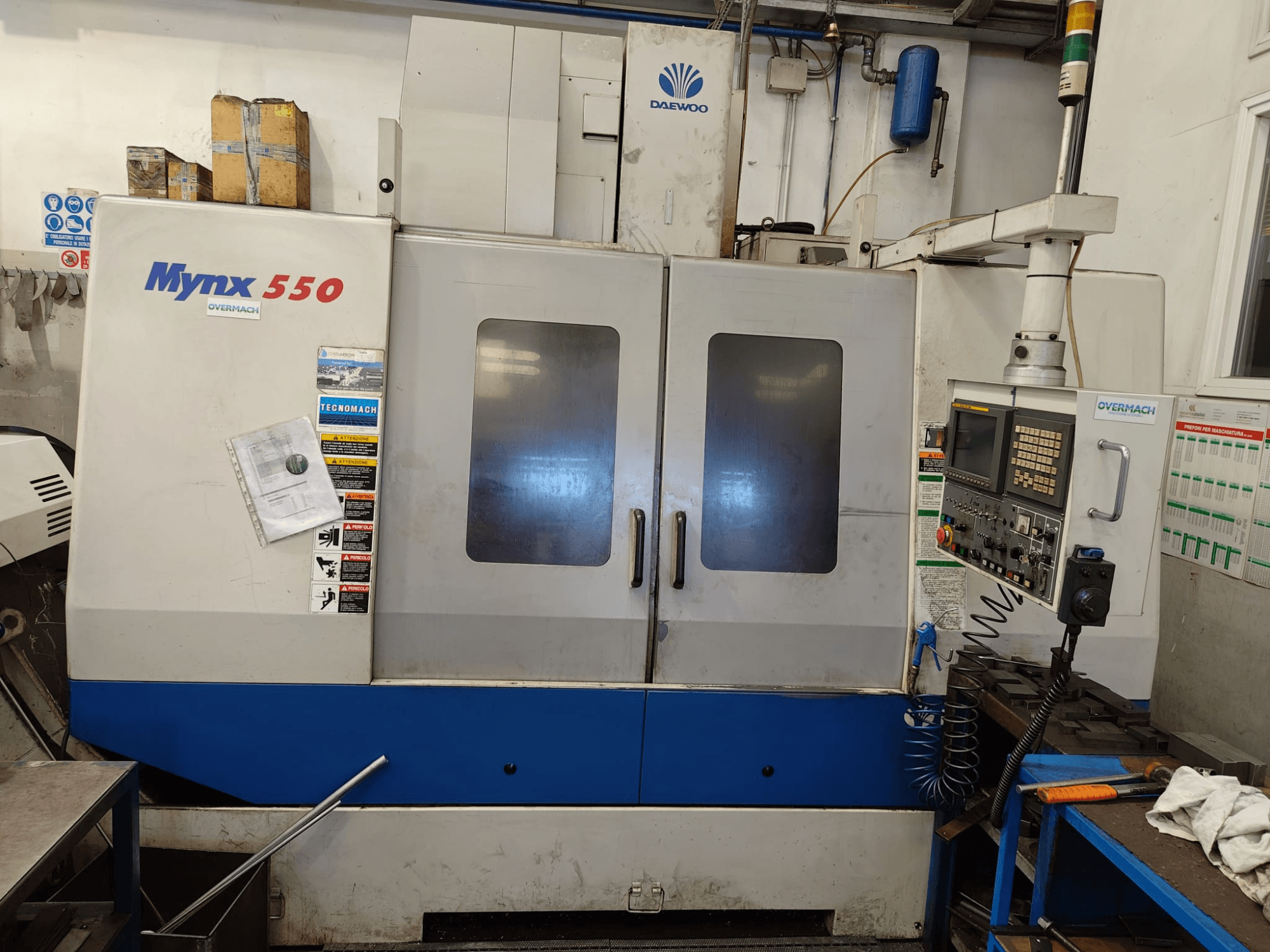 Centro di lavorazione verticale DAEWOO MYNX 550, vista frontale, con pannello di controllo, due grandi porte ed etichette di sicurezza.