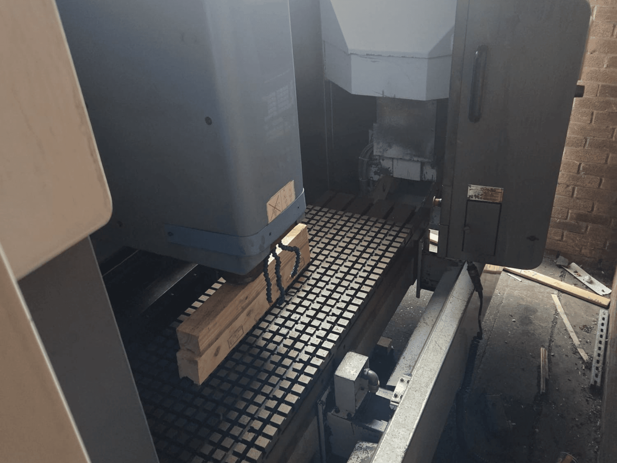 Vista frontale della macchina CNC con tavole di legno su un tavolo a griglia, con strumenti e comandi a lato.