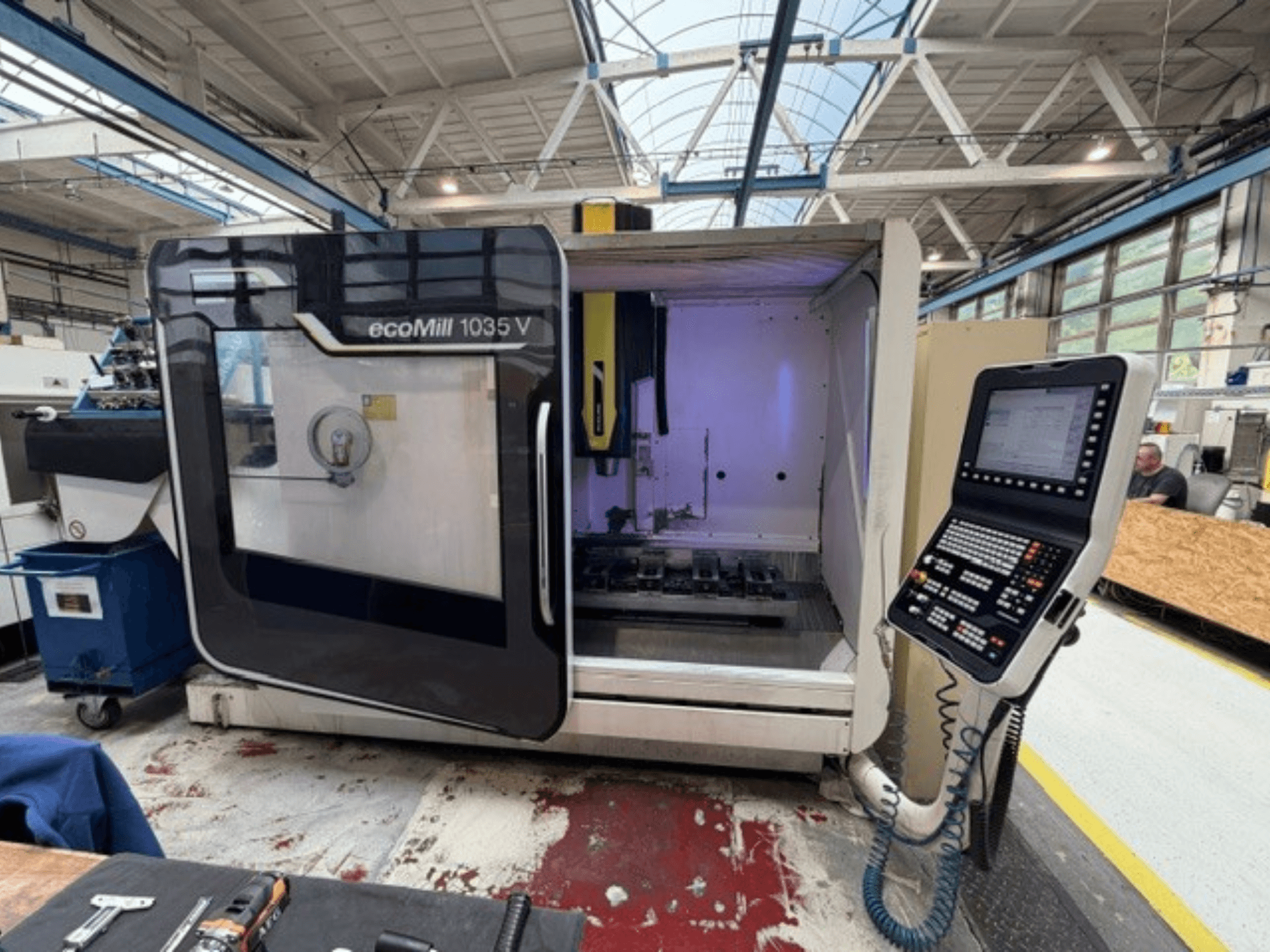 Vista frontale del centro di lavorazione verticale DMG MORI ecoMill 1035V con lo sportello aperto, che mostra il pannello di controllo e l'area di lavoro all'interno.
