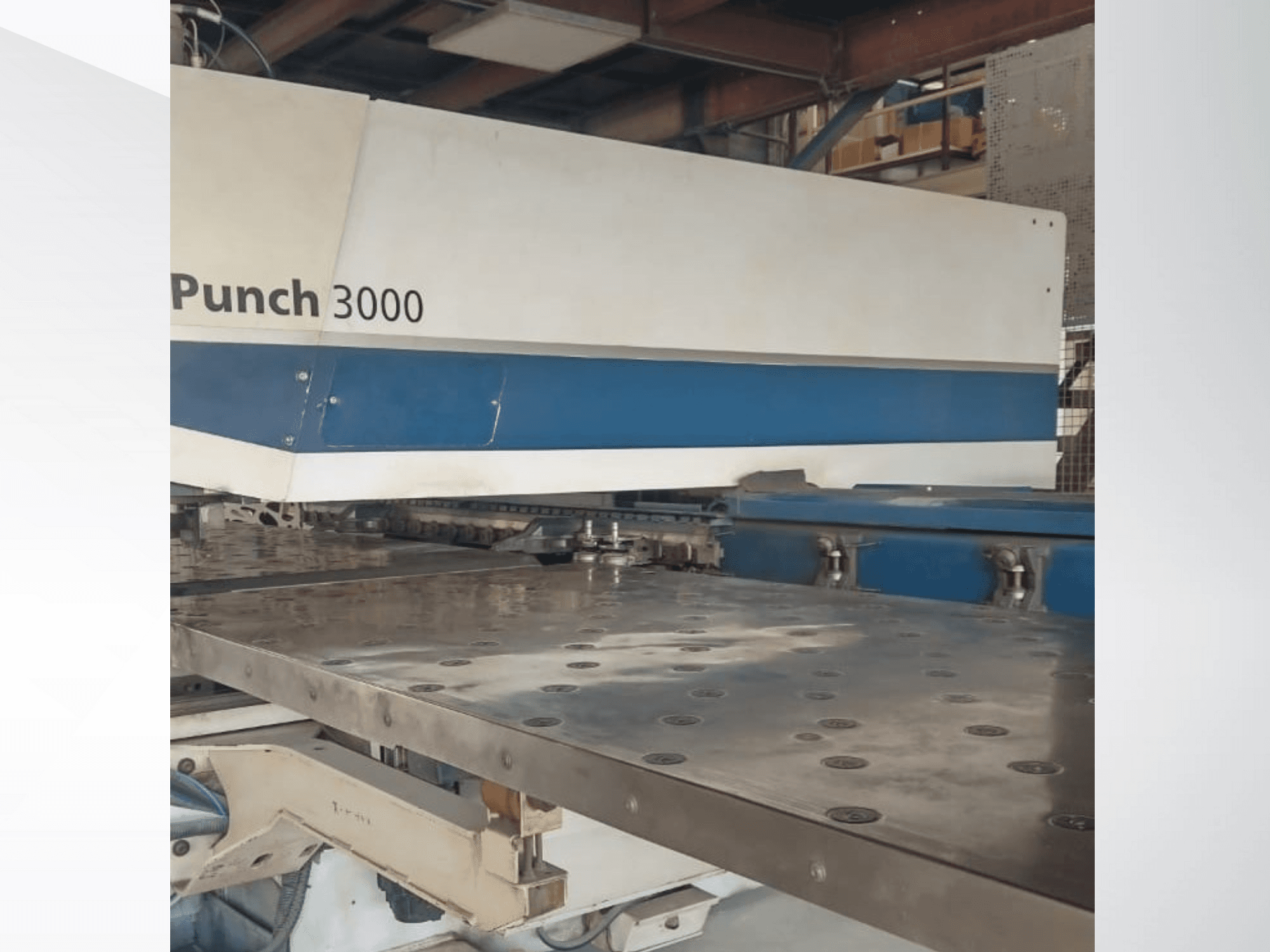 Macchina punzonatrice 3000 in un'officina, vista frontale, che mostra una grande superficie metallica piana con più fori di punzonatura.