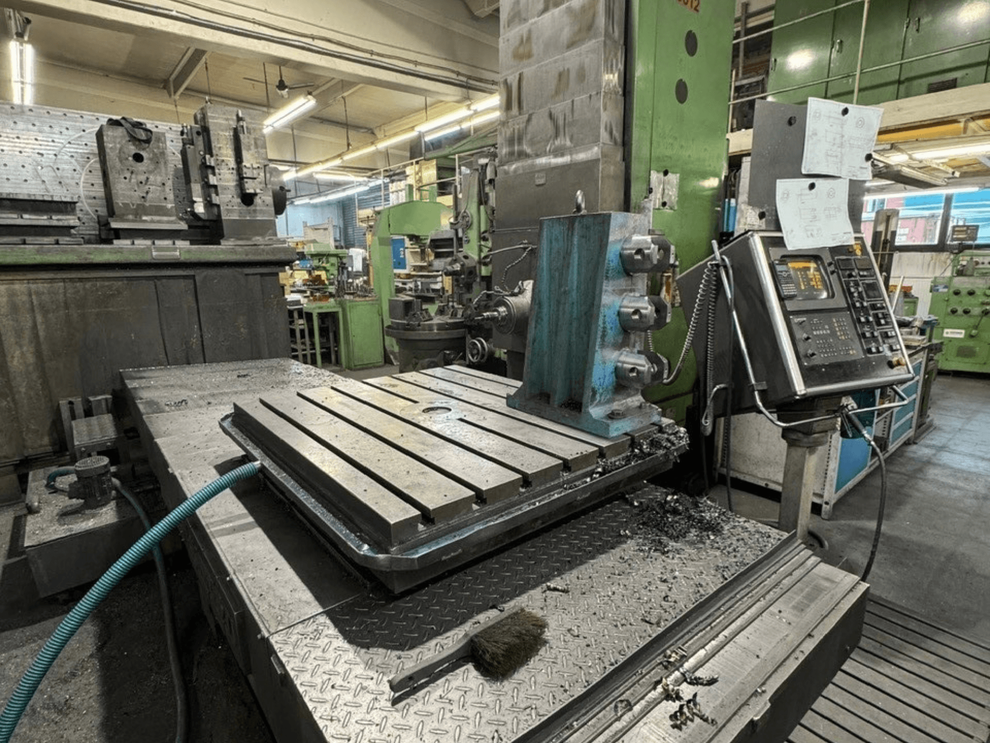Alesatrice JUARISTI 12/TS1.7 in un'officina, vista laterale che mostra il piano di lavoro in metallo con scanalature e il pannello di controllo nelle vicinanze.