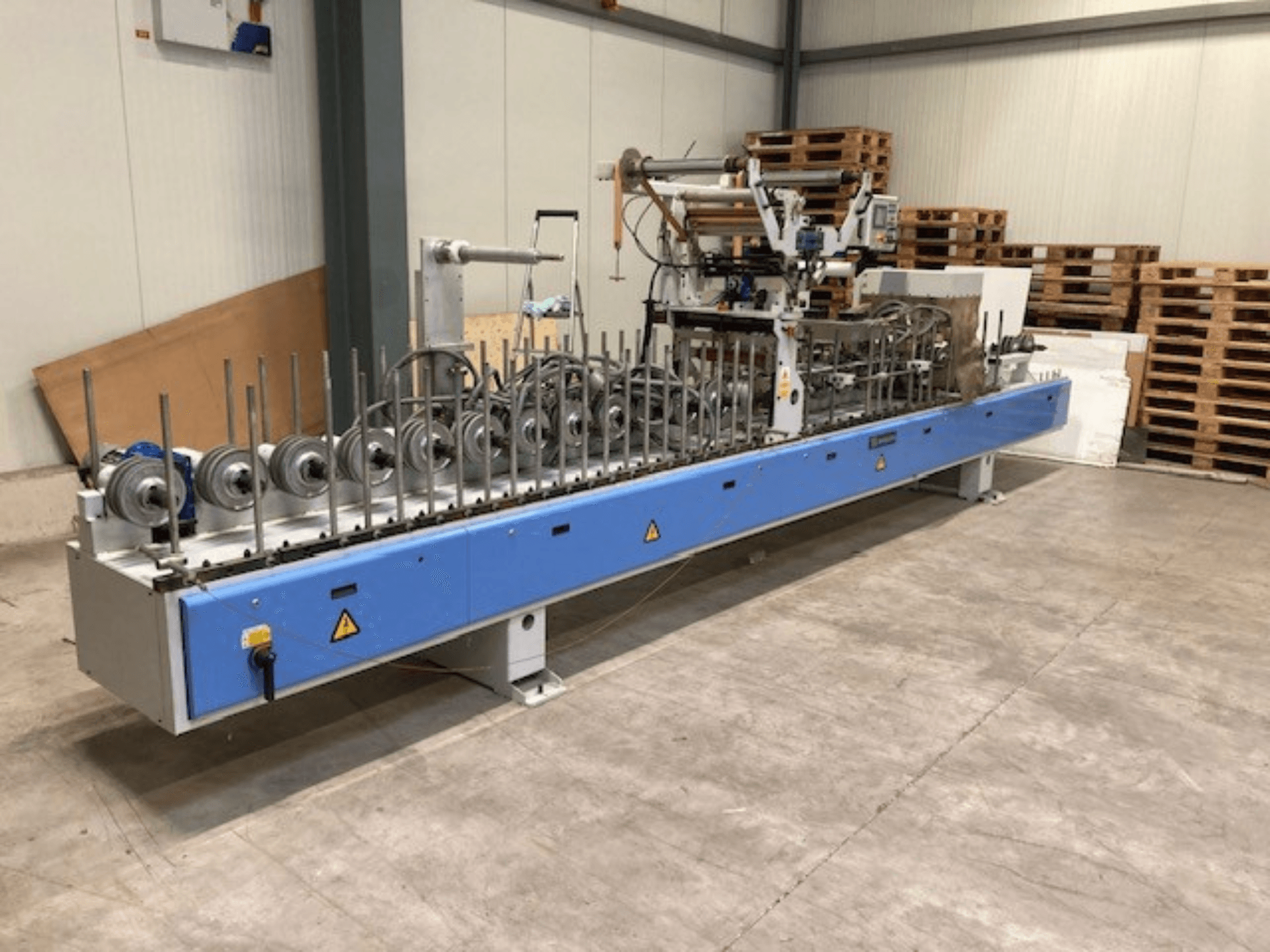 Pressa di laminazione Barberan PUR 46 L, vista frontale, con rulli multipli e base blu in un magazzino.