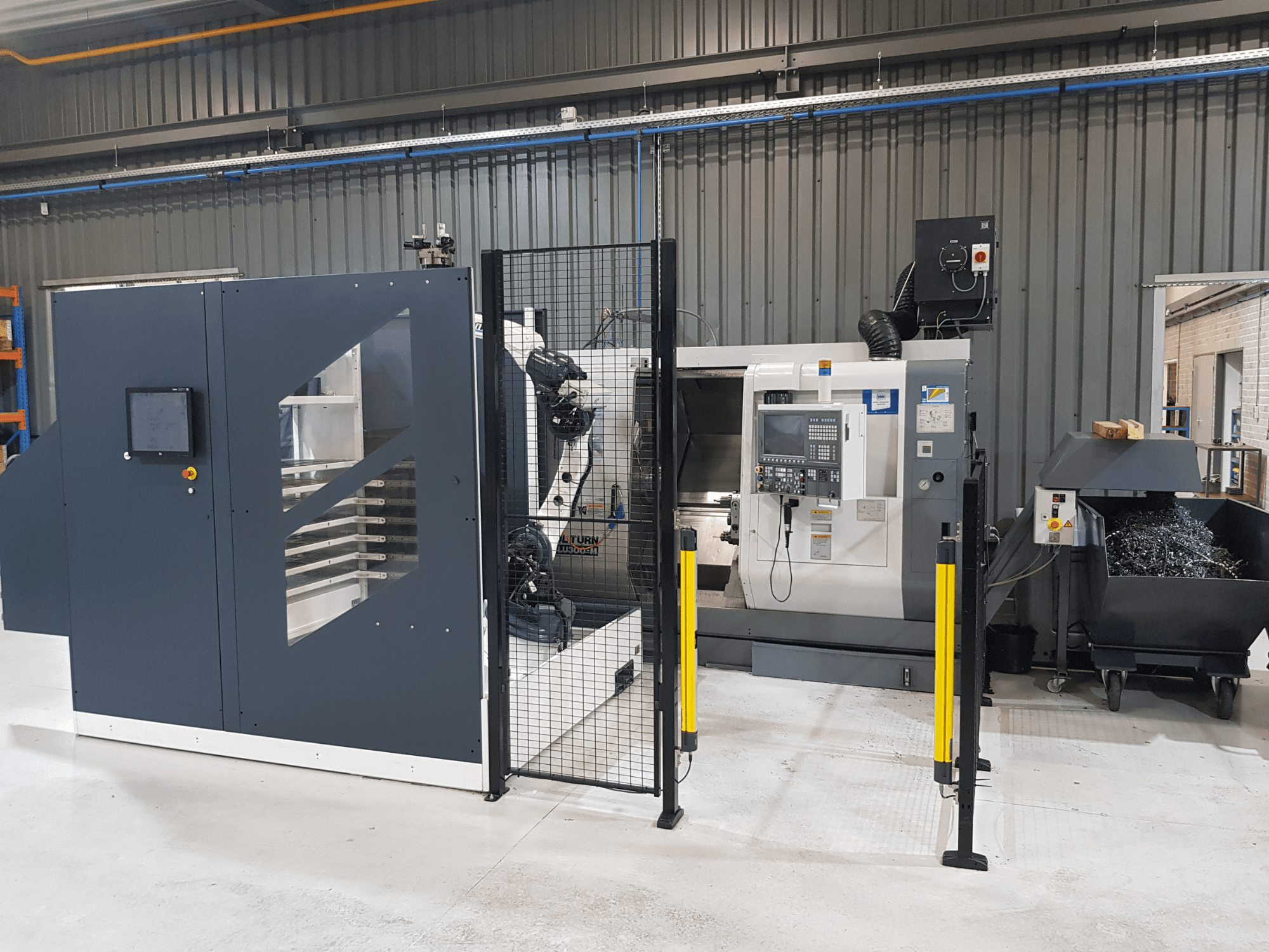 Tornio automatico e macchina CNC ALTURN in un ambiente di fabbrica; vista frontale con pannello di controllo e recinzione di sicurezza visibili.
