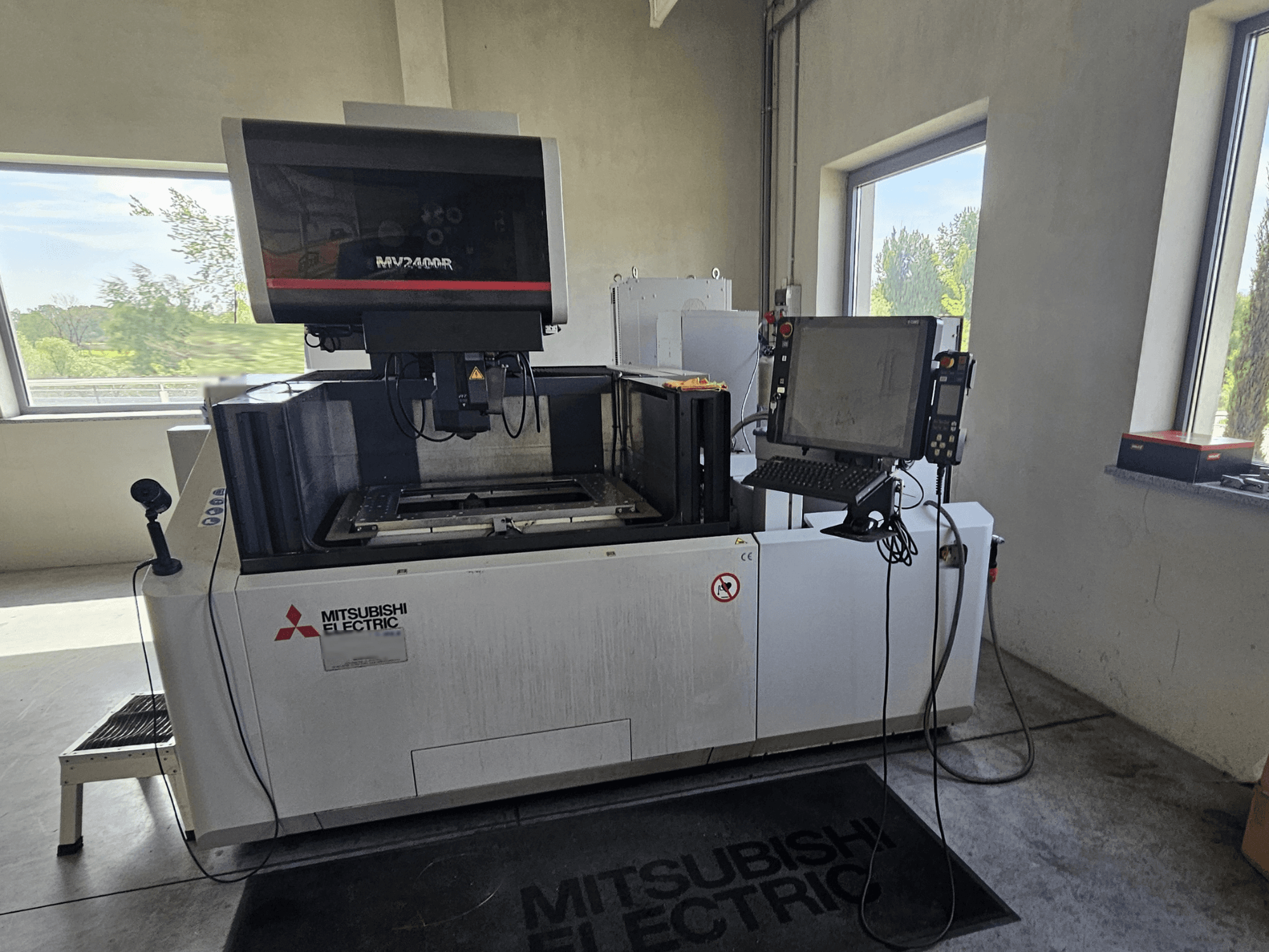 Macchina per elettroerosione a filo Mitsubishi MV2400R in un'officina, con pannello di controllo touchscreen e area di lavoro.