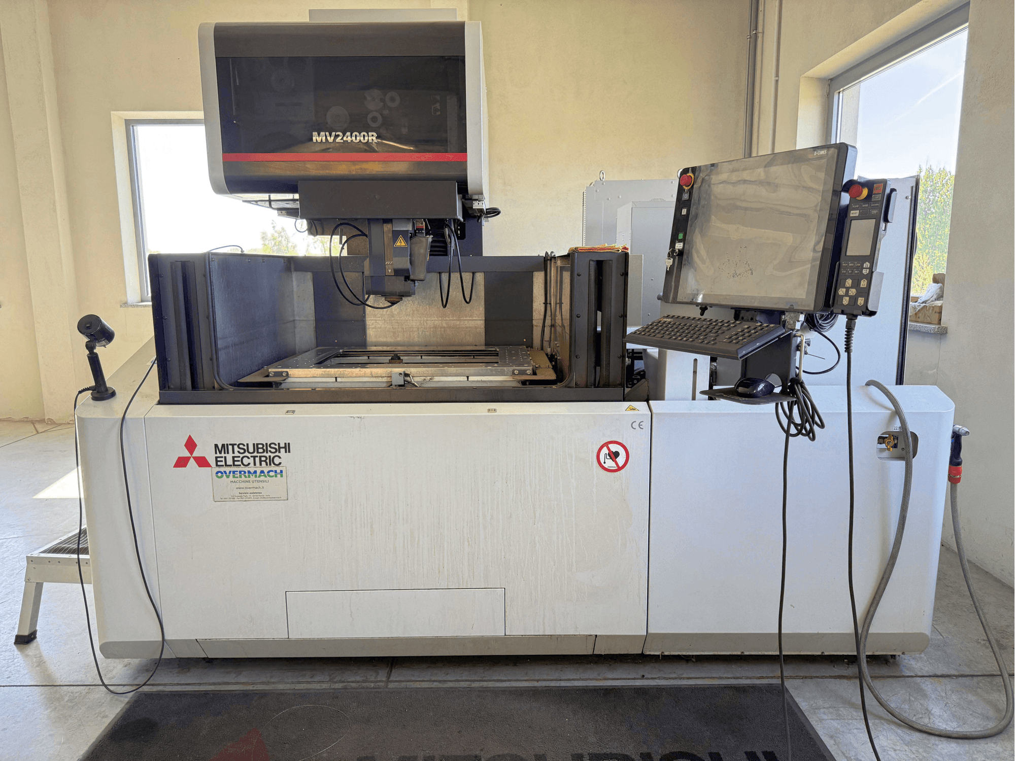 Macchina per elettroerosione a filo Mitsubishi MV2400R vista frontale, con pannello di controllo, area di lavoro e segnaletica di sicurezza.