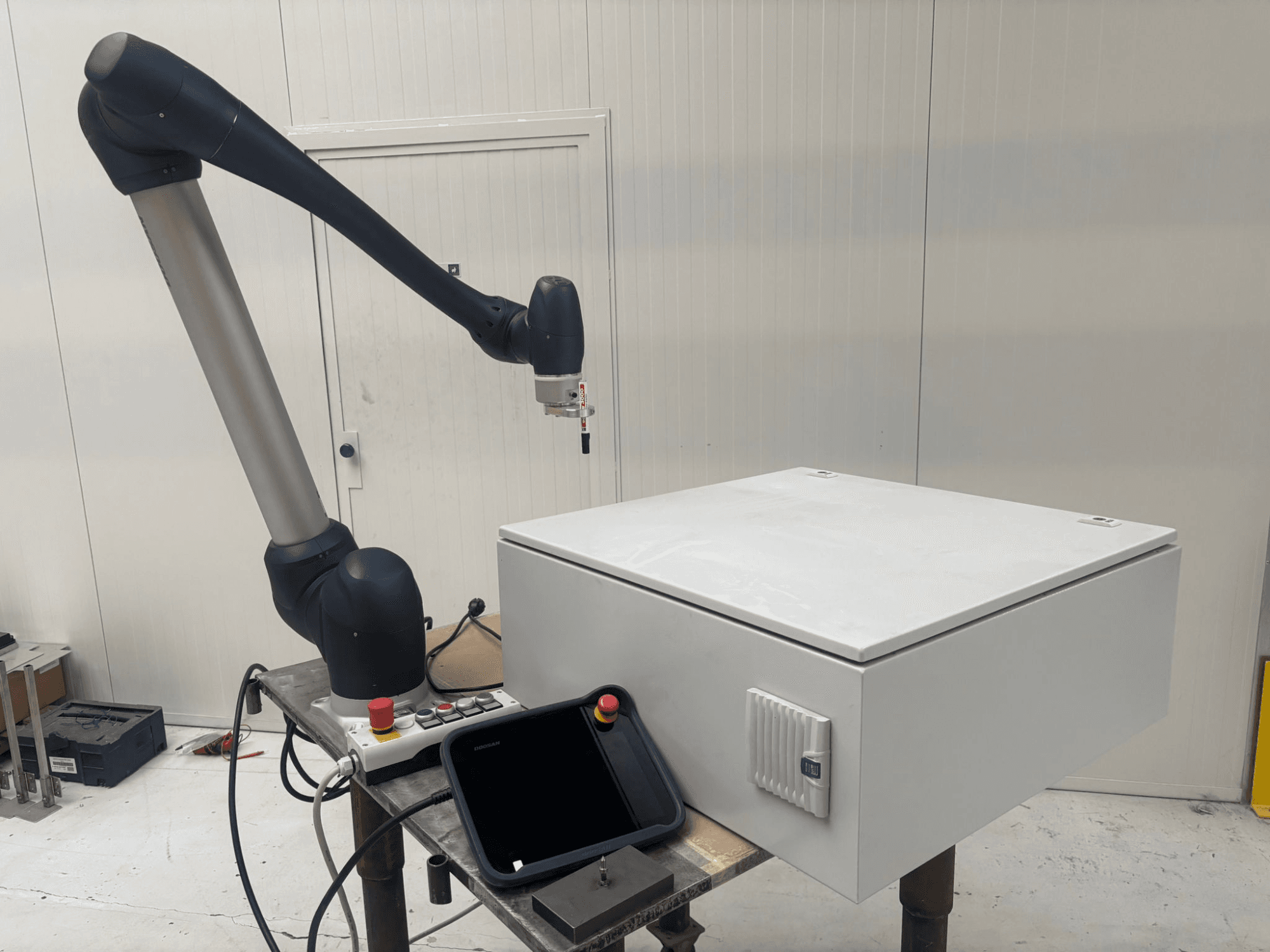 Robot collaborativo DOOSAN M0617 in vista laterale, con braccio robotico esteso sopra un'interfaccia di controllo e una scatola bianca su un tavolo.