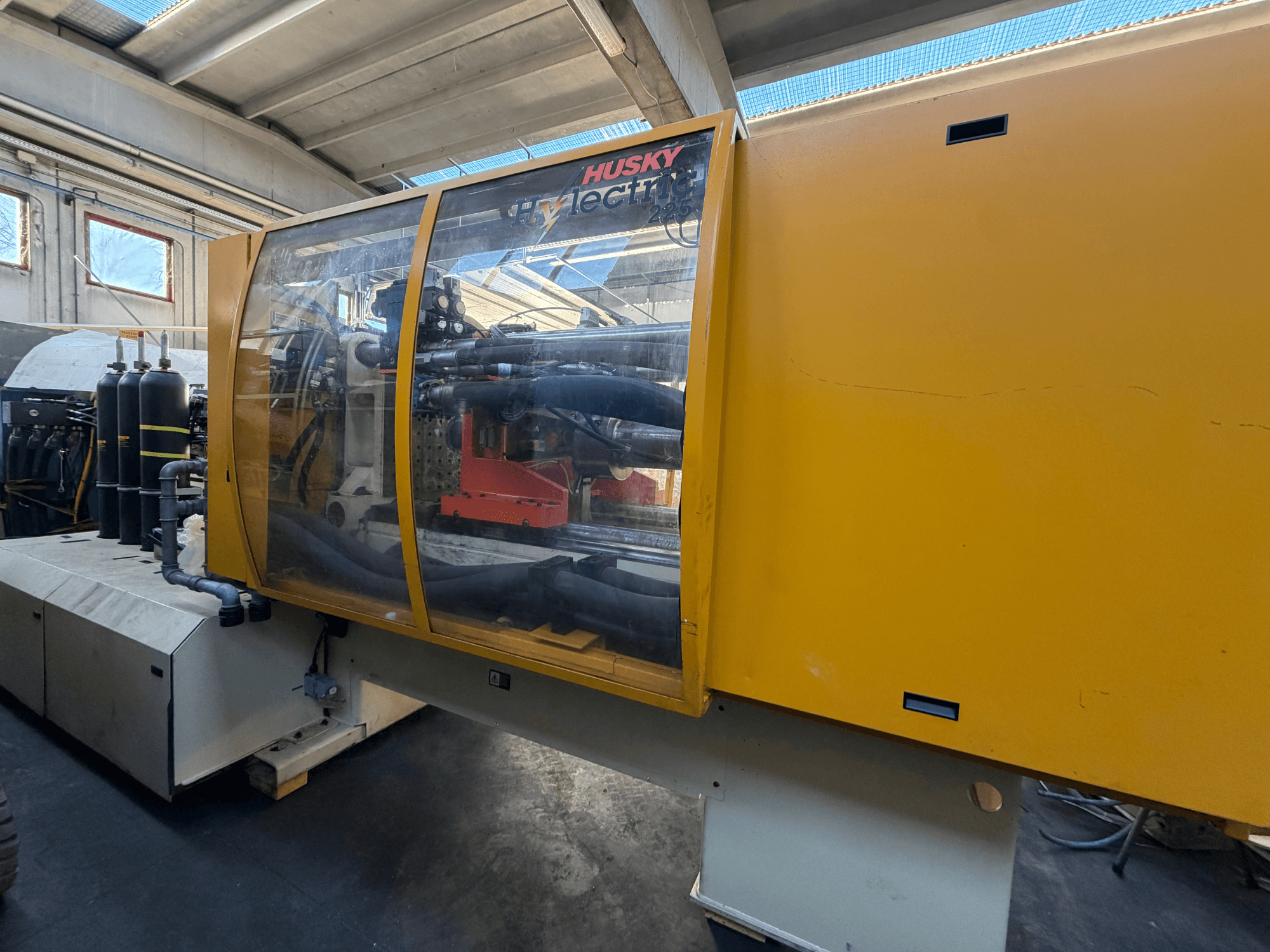 Pressa a iniezione elettrica Husky HL225 RS65, vista frontale con carter giallo, pannello di controllo visibile e componenti idraulici.