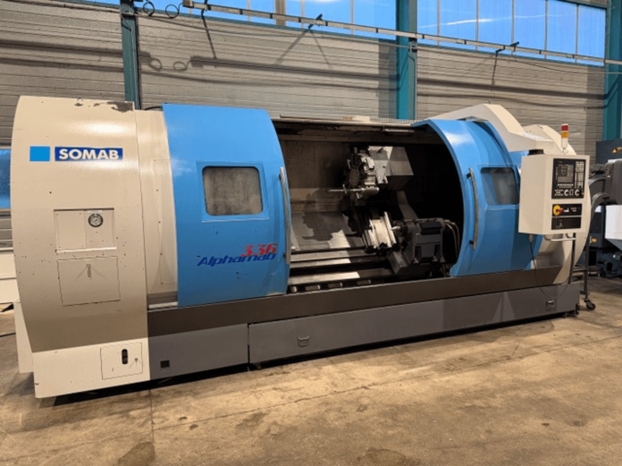 Tornio CNC SOMAB Alpha 336, vista frontale, con involucro blu e grigio e pannello di controllo laterale per il funzionamento.