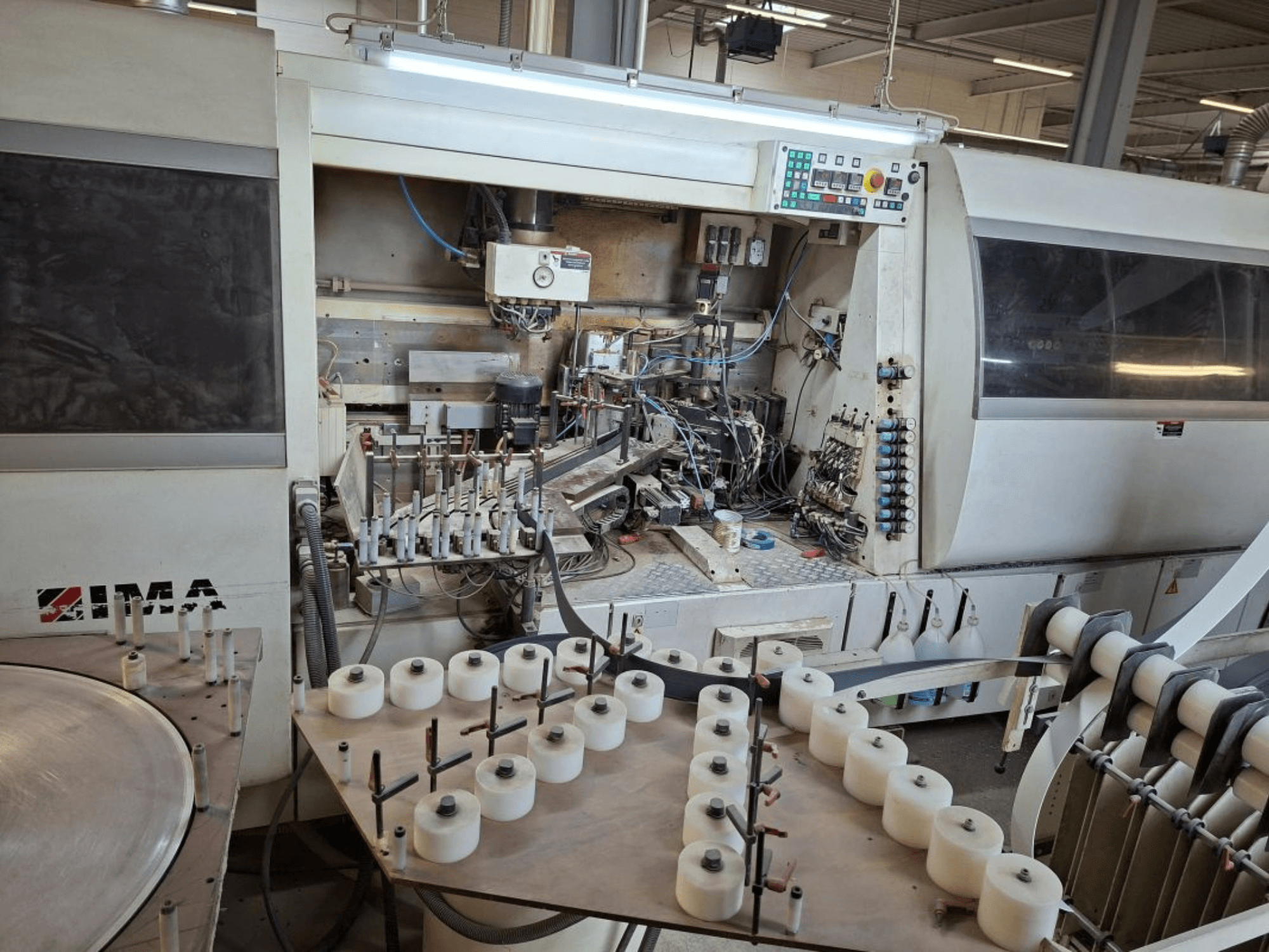 Macchinario IMA visto di lato, con componenti meccanici complessi e un tavolo rotondo con bobine bianche.