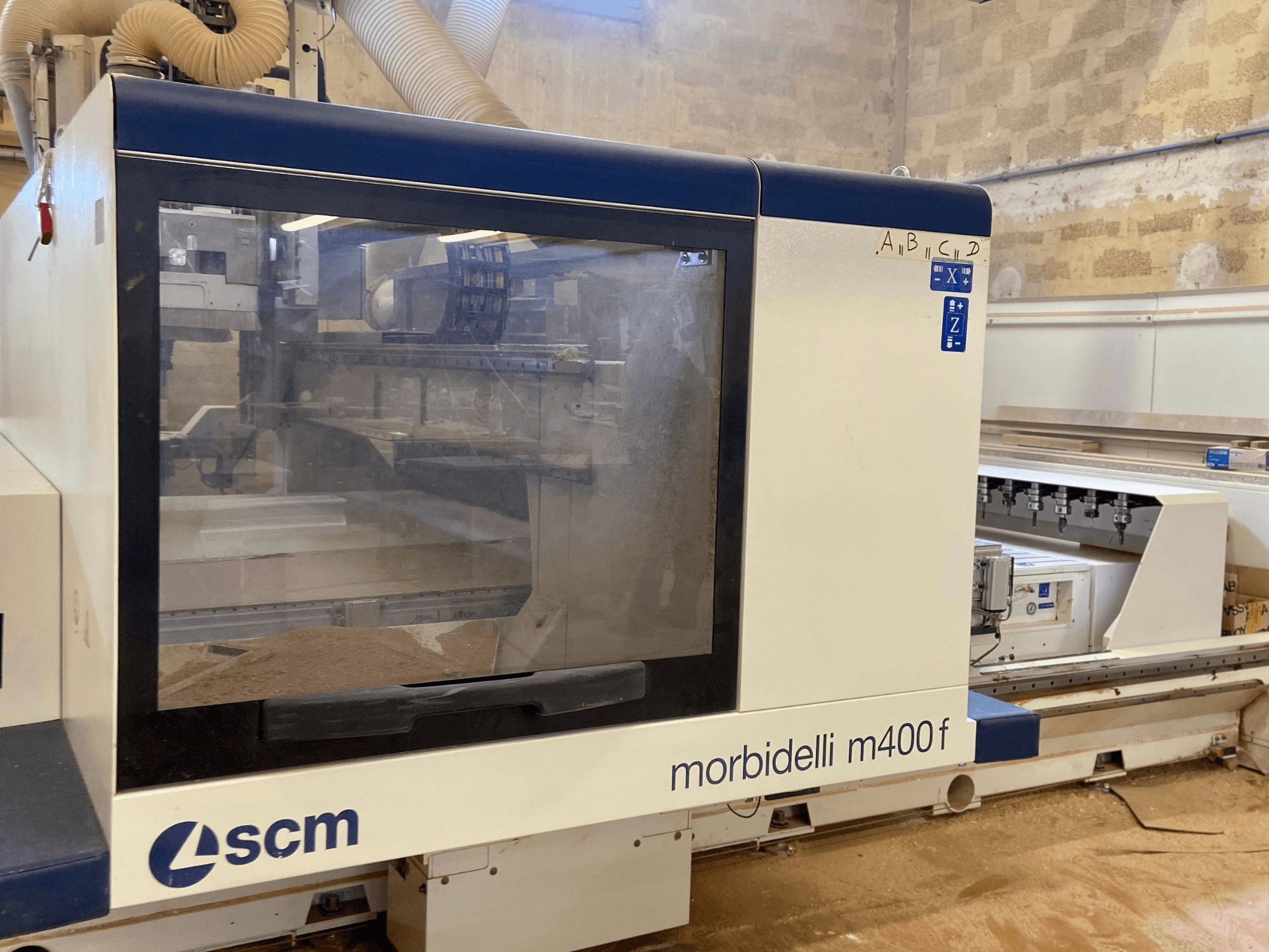 Macchina CNC SCM Morbidelli M400F, vista frontale, con pannello di controllo e segatura visibile sul pavimento.
