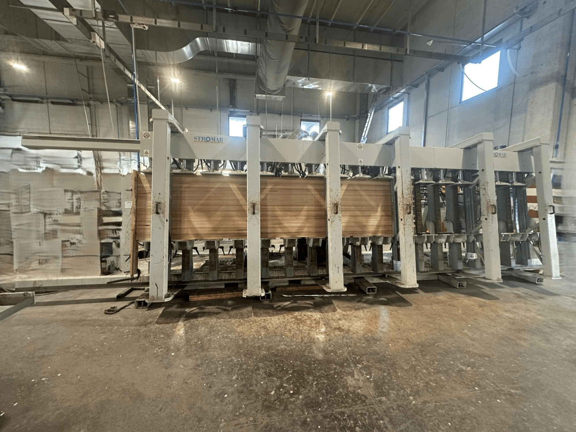 Macchina industriale STROMAB in un magazzino, vista frontale, con pannelli di legno in lavorazione, che mostra la struttura metallica e le parti meccaniche.
