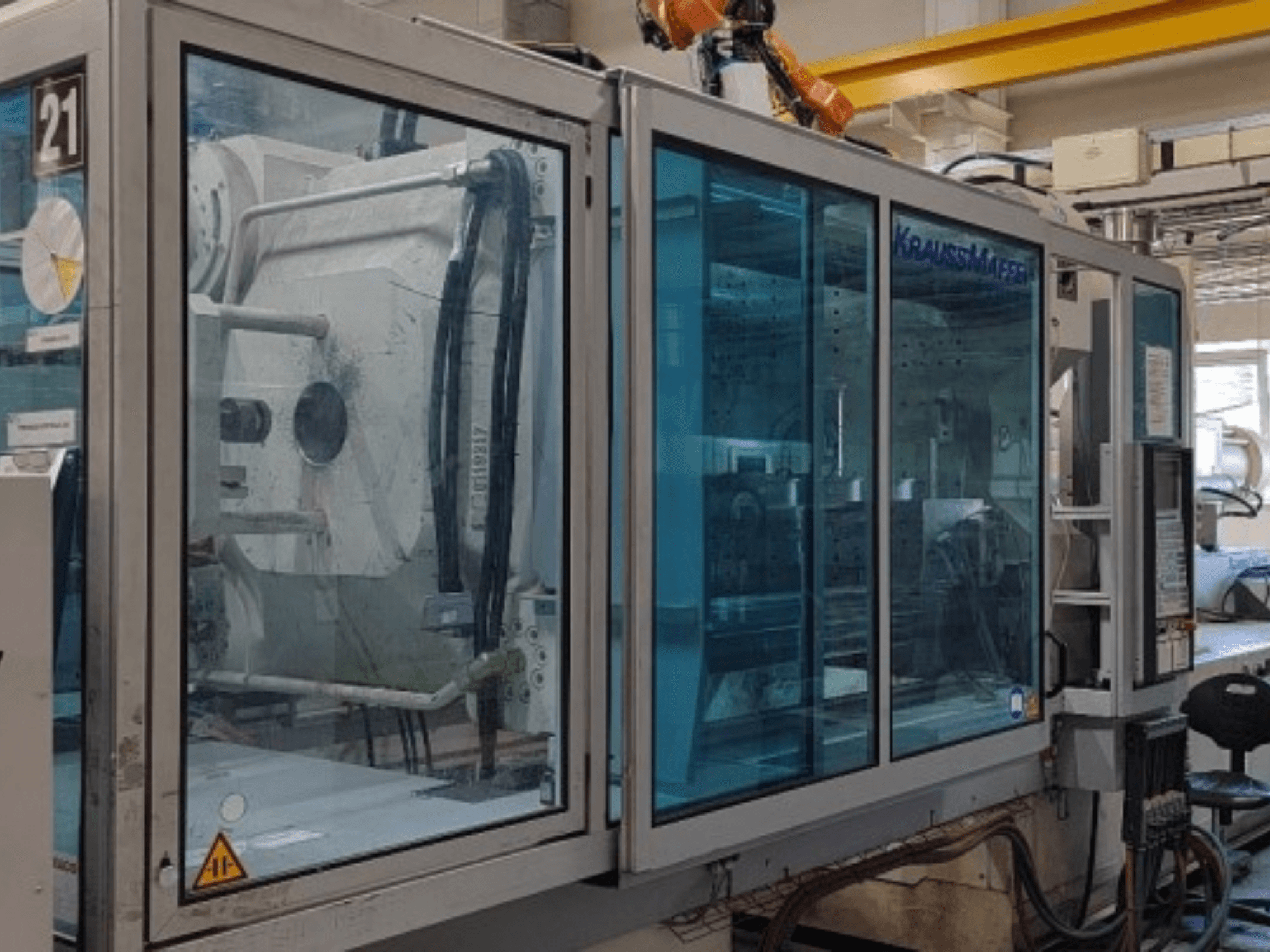 Macchina per lo stampaggio a iniezione idraulica Krauss Maffei KM 575-2700 C2, vista laterale, dotata di pannelli di sicurezza trasparenti e pannello di controllo.